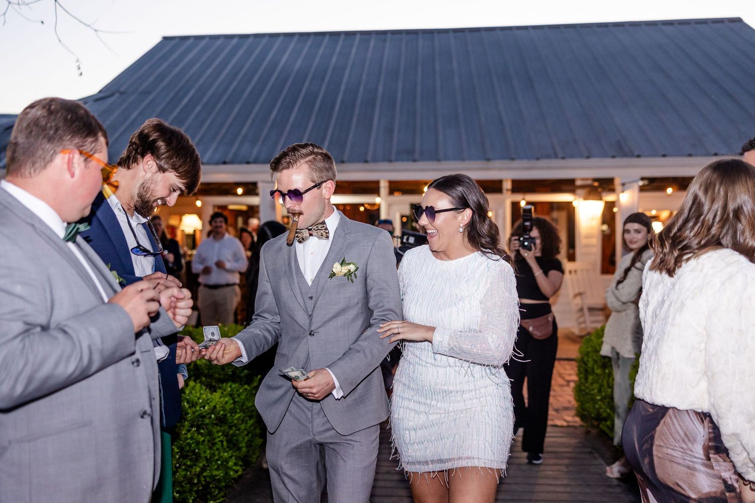 Wedding guests gather outside a venue with a dark metal roof during a celebration.