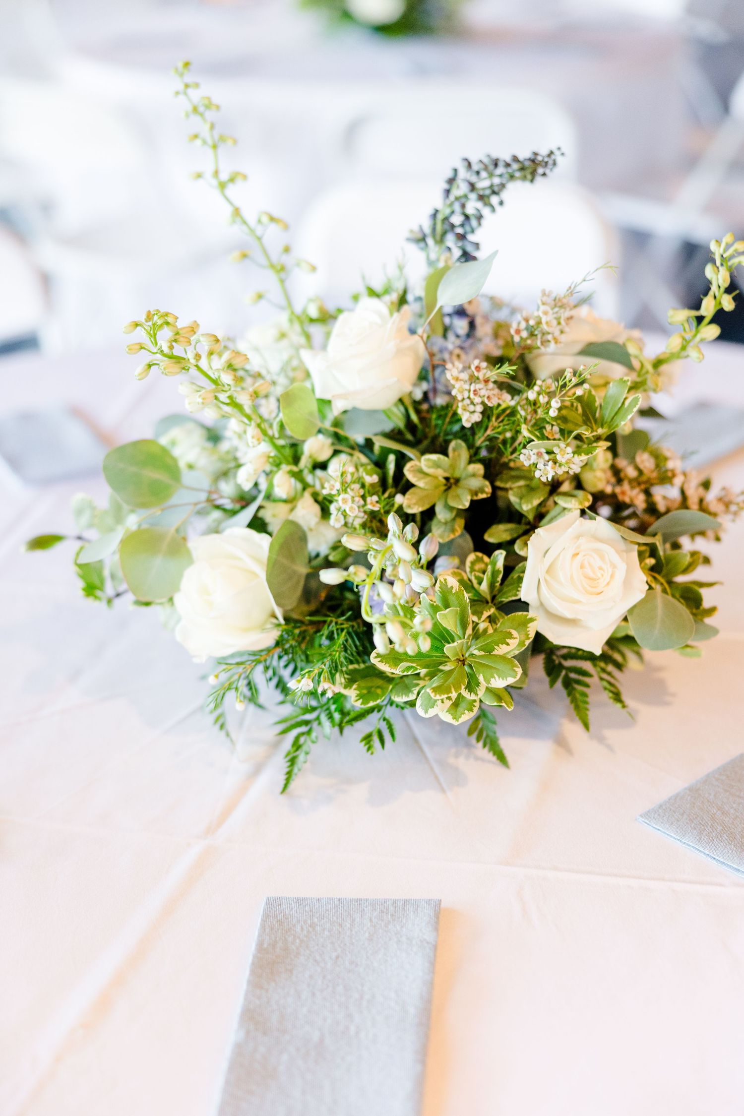 Delicate wedding table arrangement featuring peach roses and greenery on white linens.