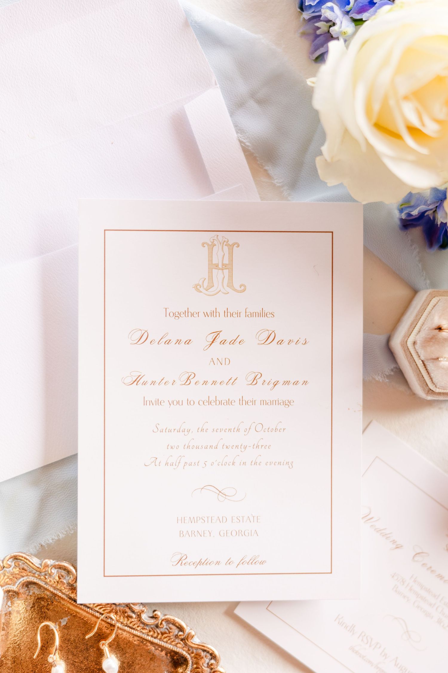Elegant blush wedding invitation with monogram design surrounded by roses and delicate flowers.