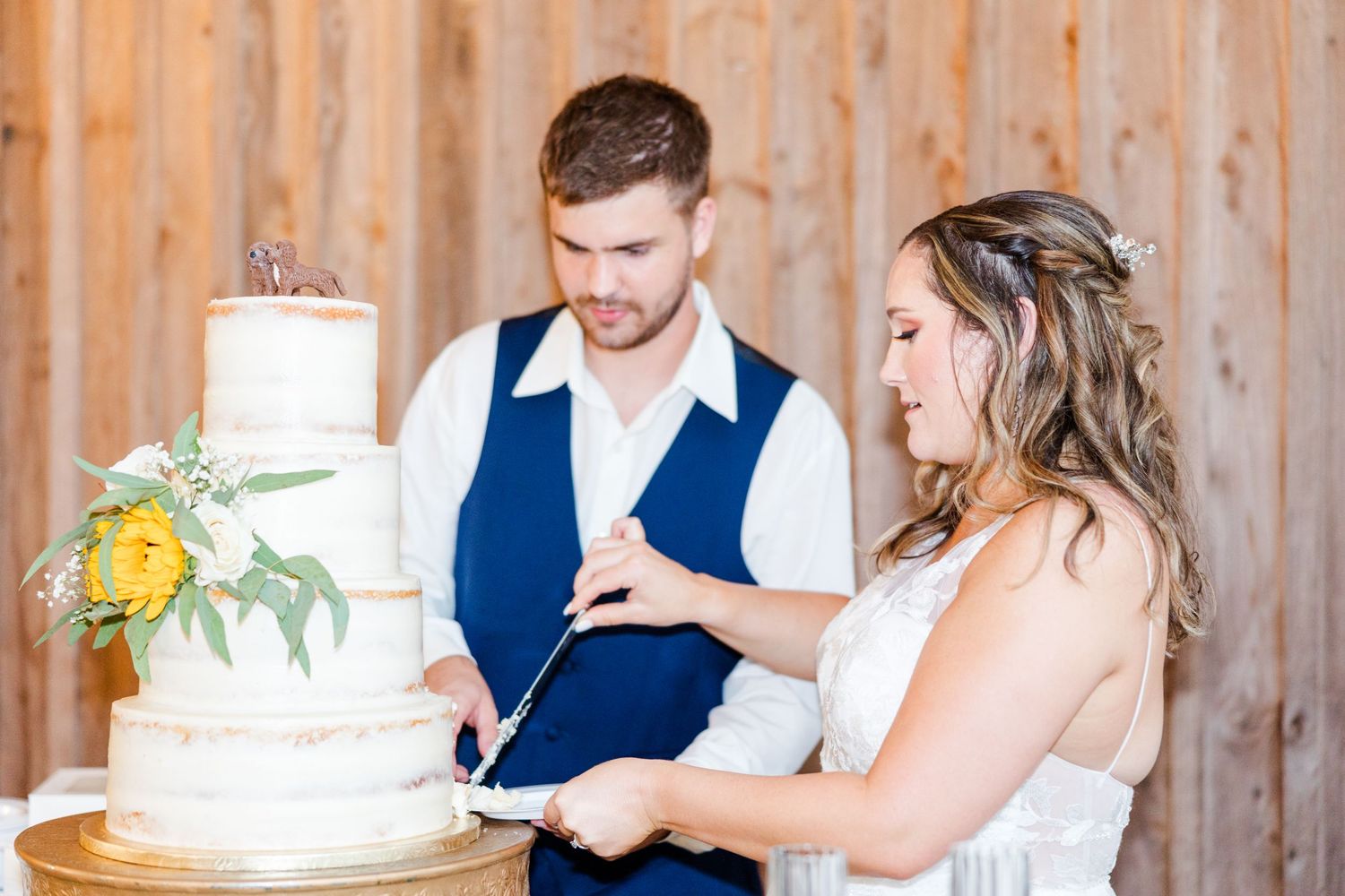 Newlyweds share playful cake cutting moment at rustic wooden venue.