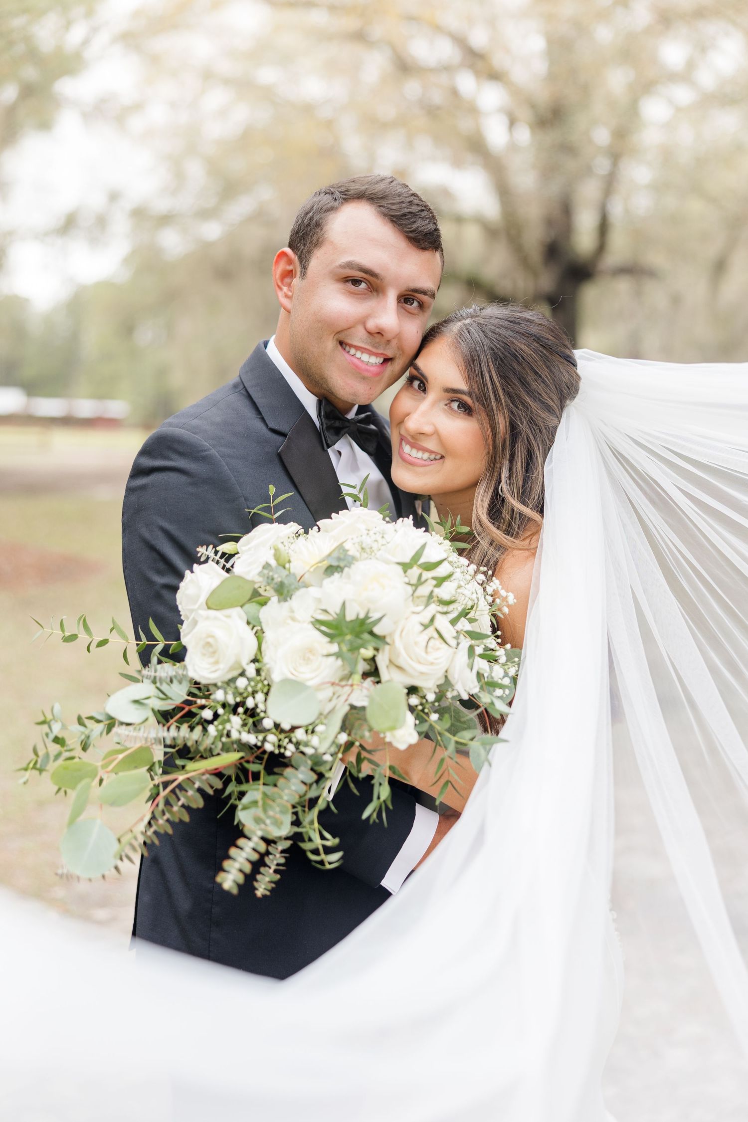 A joyful wedding portrait featuring a couple with a beautiful white and green bouquet against a natural backdrop.