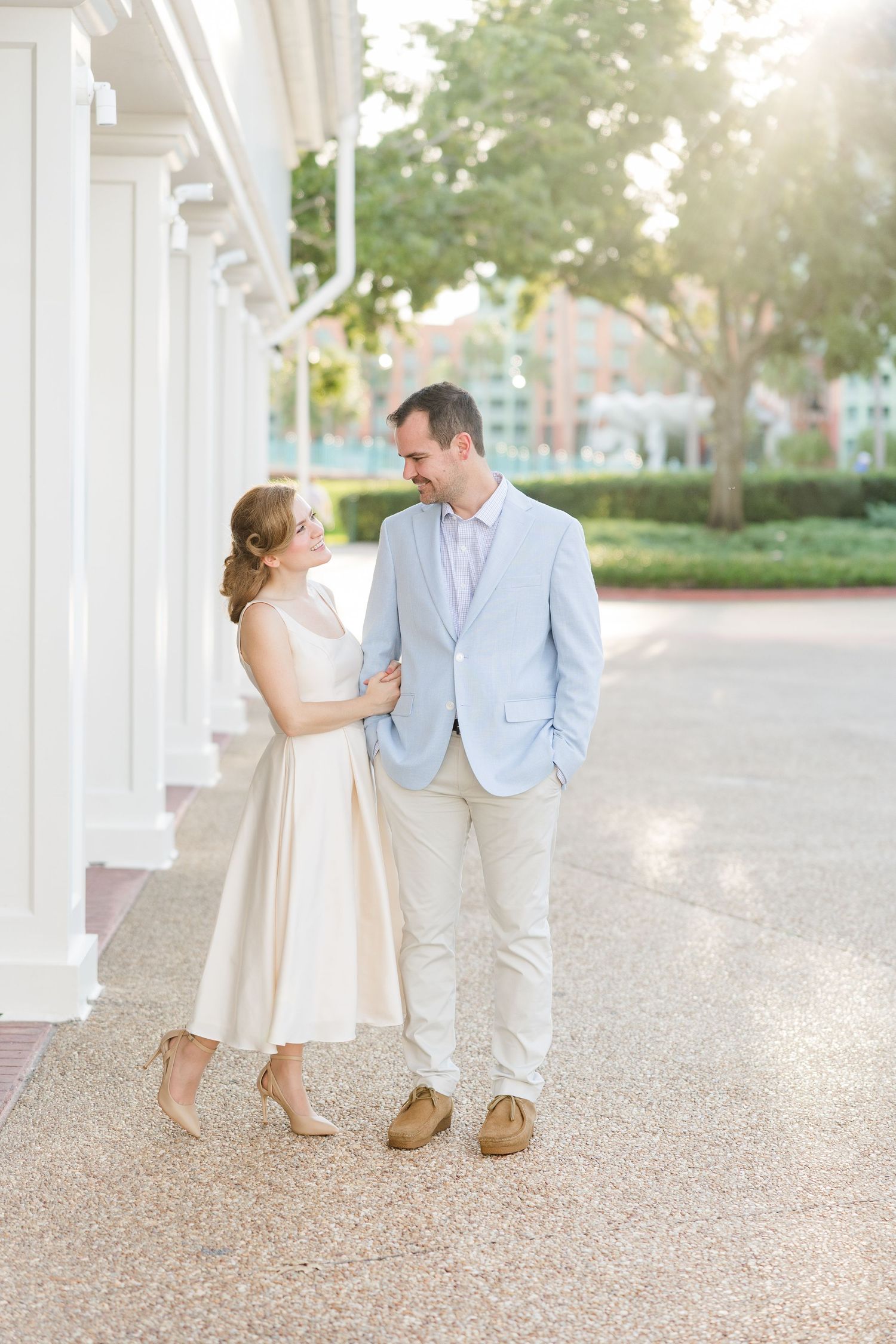 Couple in elegant attire sharing a romantic moment on a sunlit colonnade walkway.