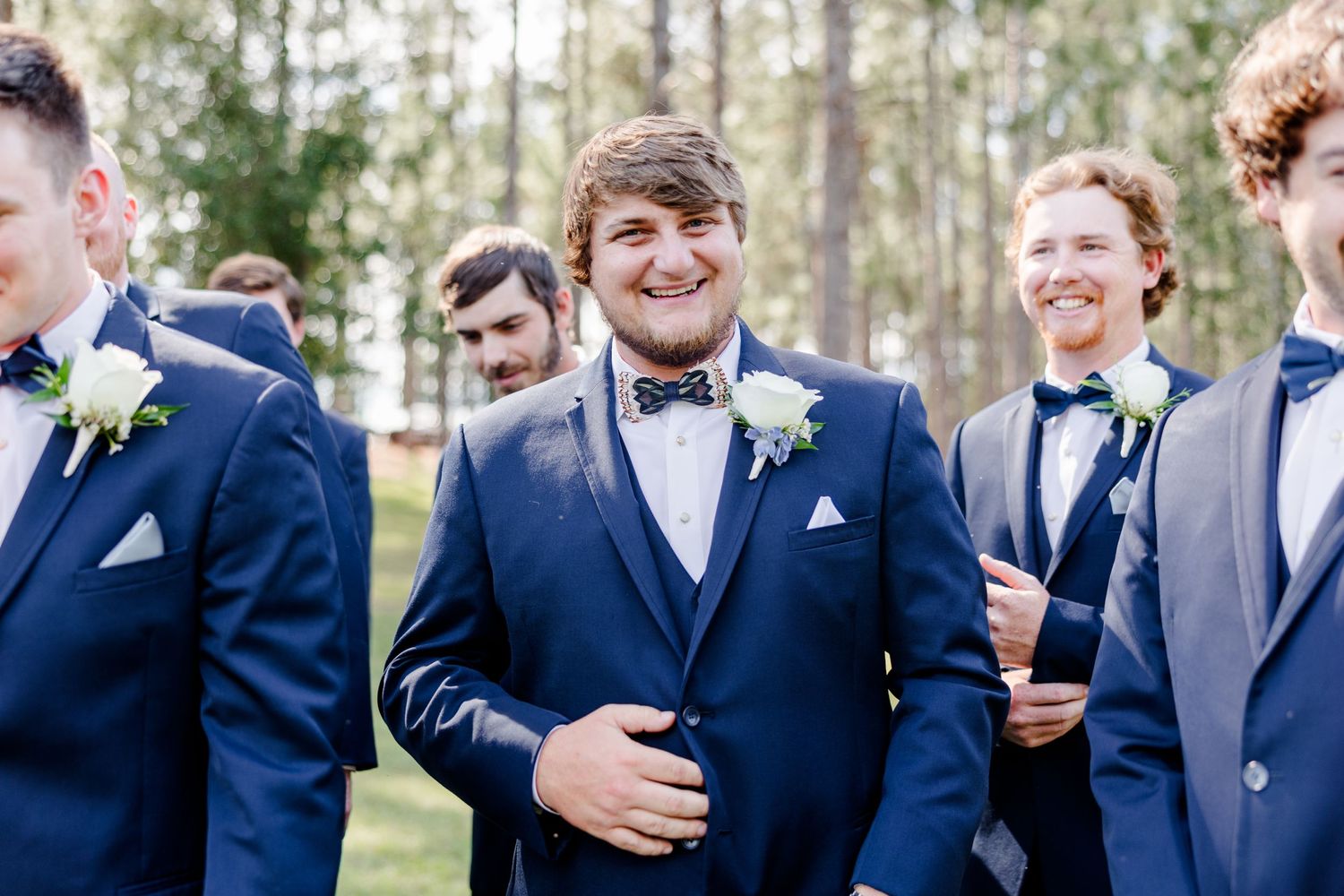 Groomsmen in navy suits share laughs during outdoor wedding photo session.