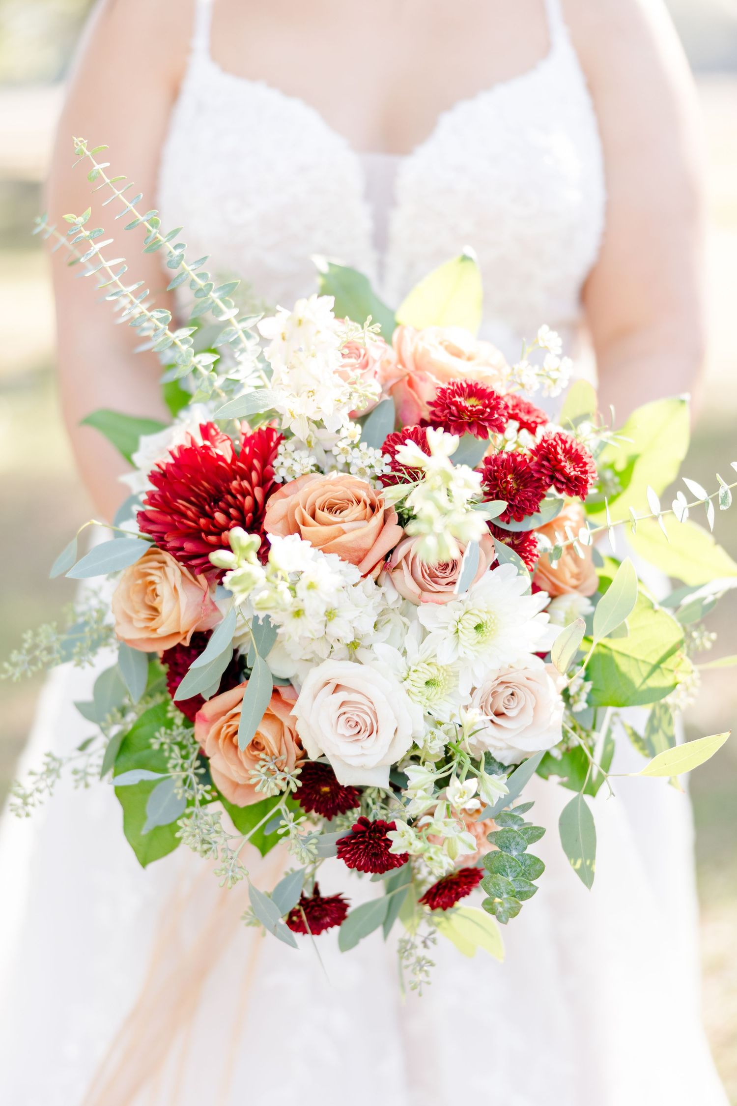Bridal bouquet features blush roses and deep red dahlias with mixed greenery.