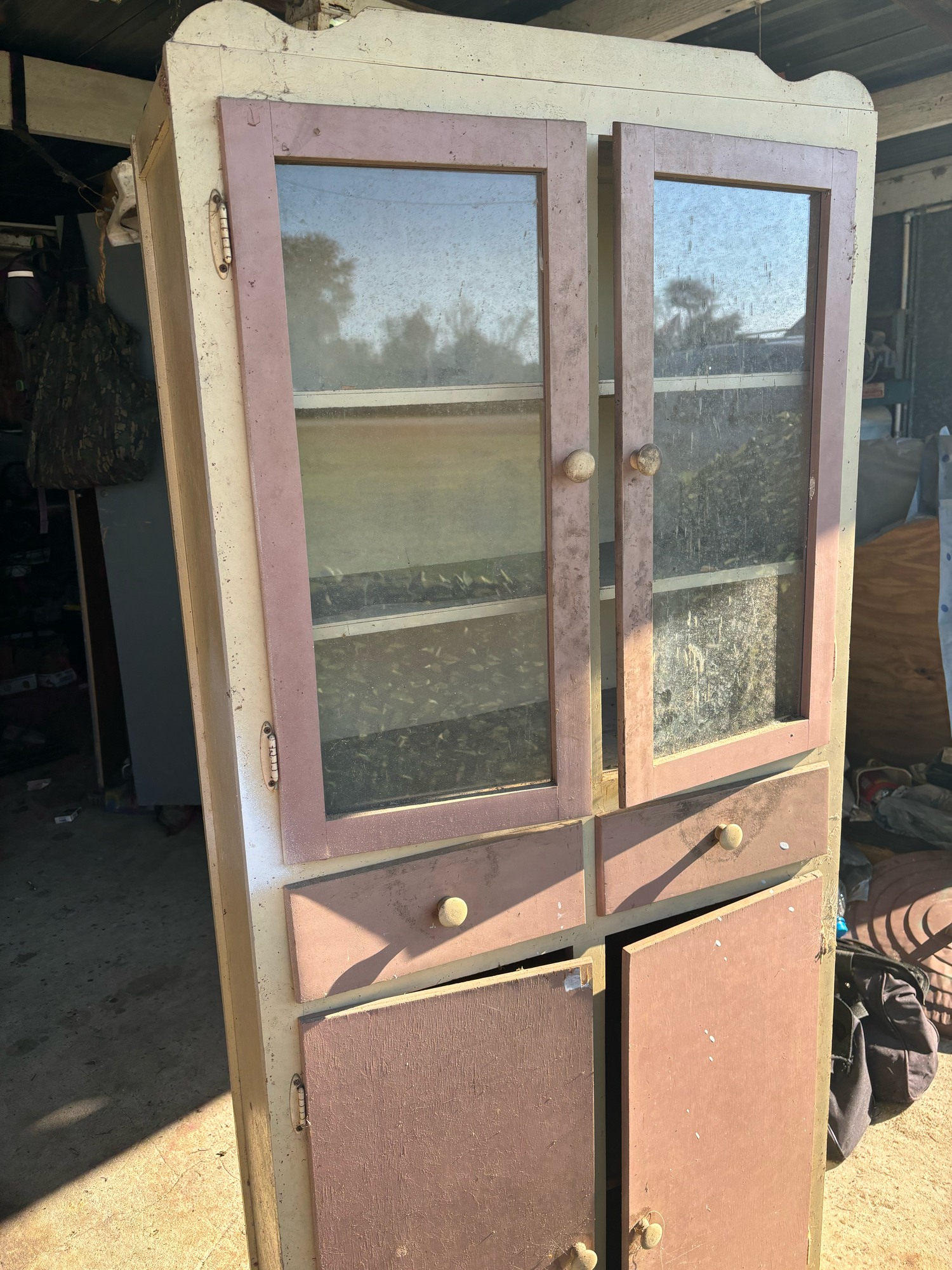 Vintage wooden cabinet with glass doors, drawer, and lower storage, showing aged pink and white paint patina.