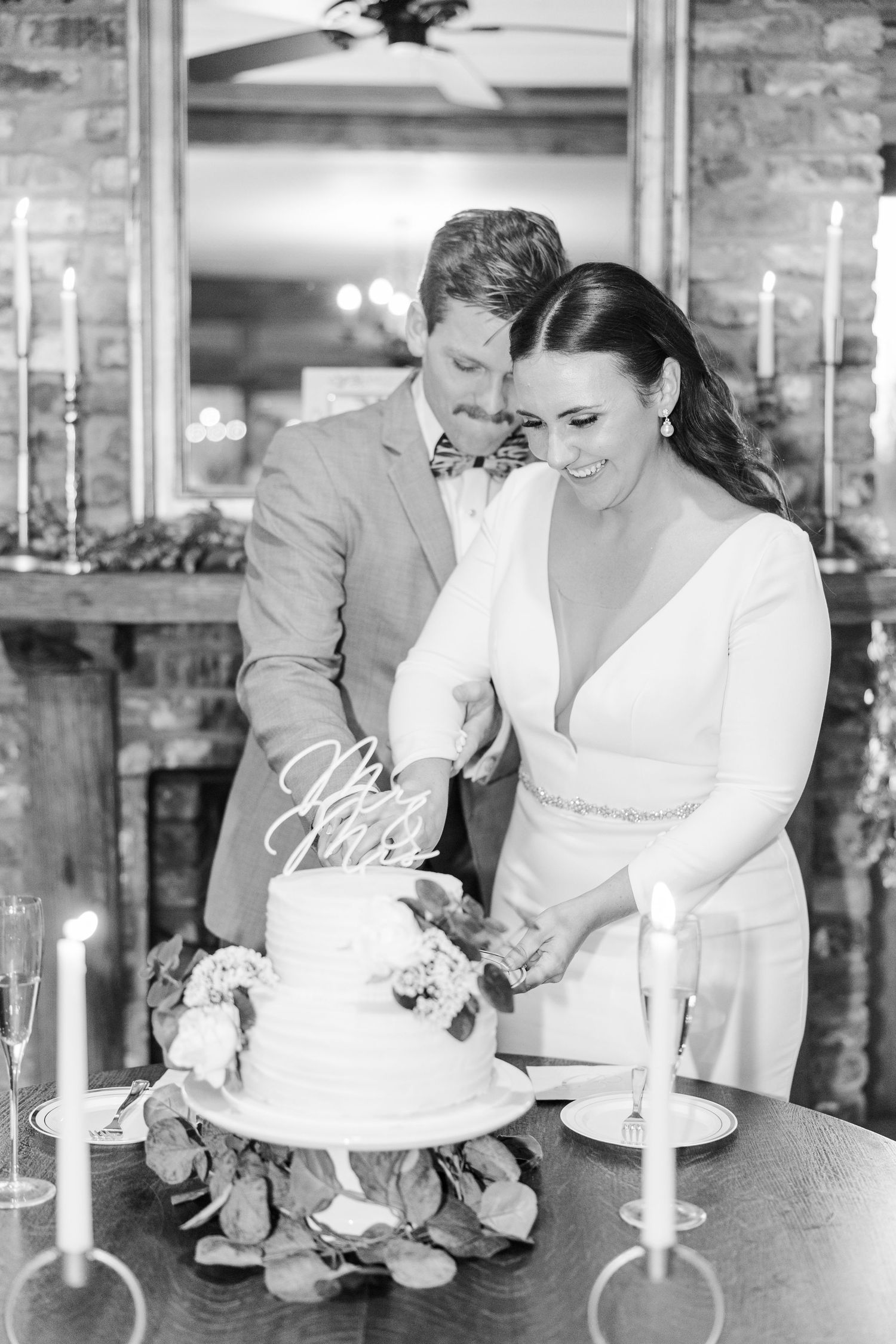 Black and white photo of wedding cake cutting at rustic reception venue.