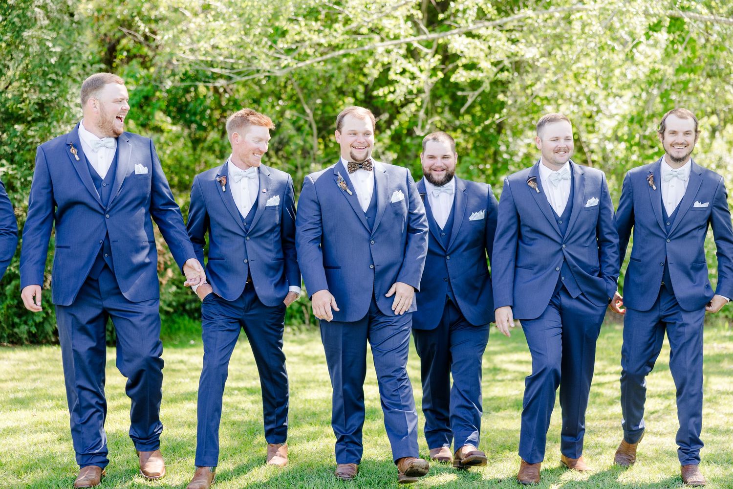 Groomsmen in matching navy suits lined up in garden setting.
