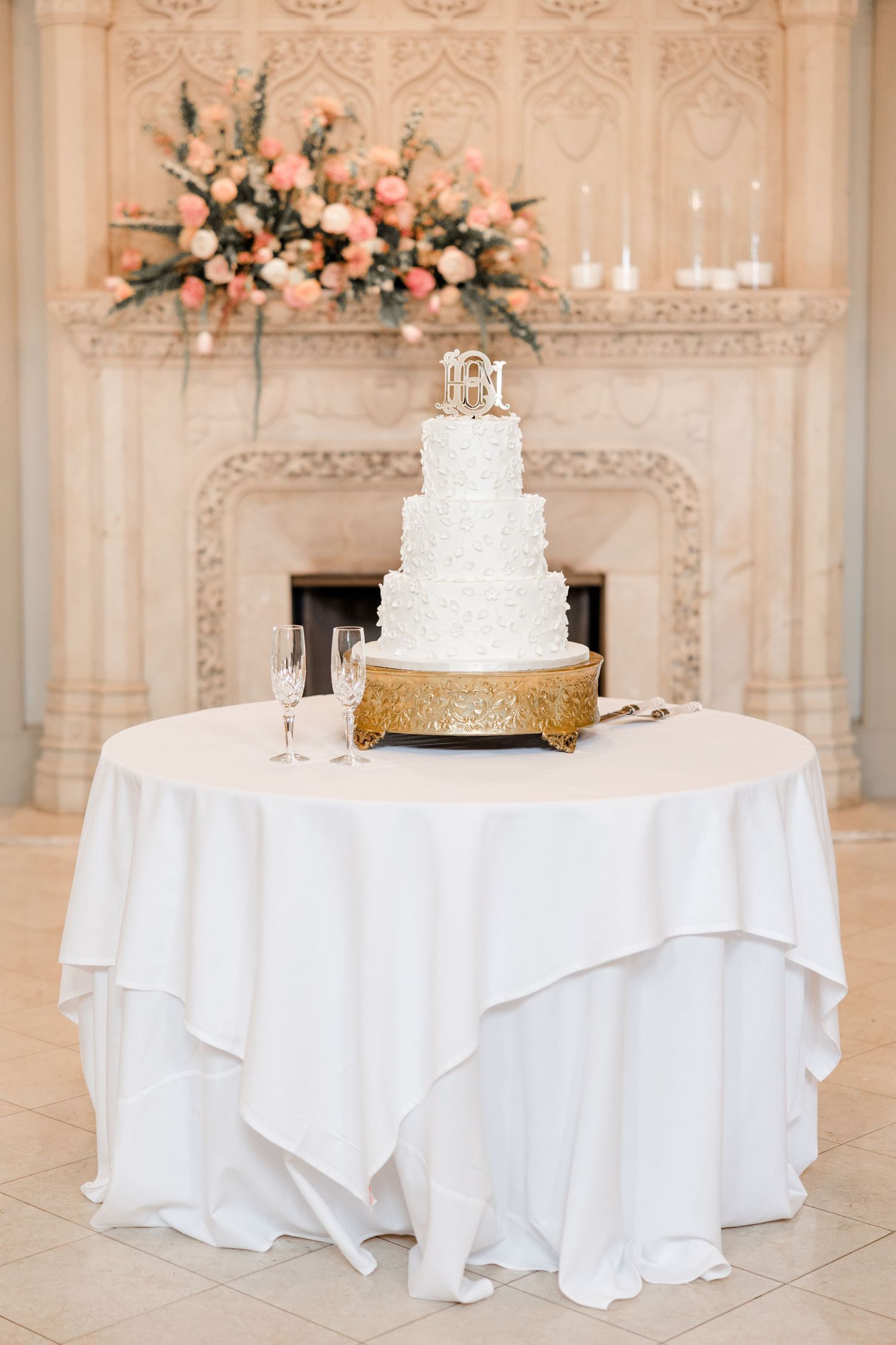 Elegant wedding reception tables with white linens and tiered cake decorated with coral flowers.