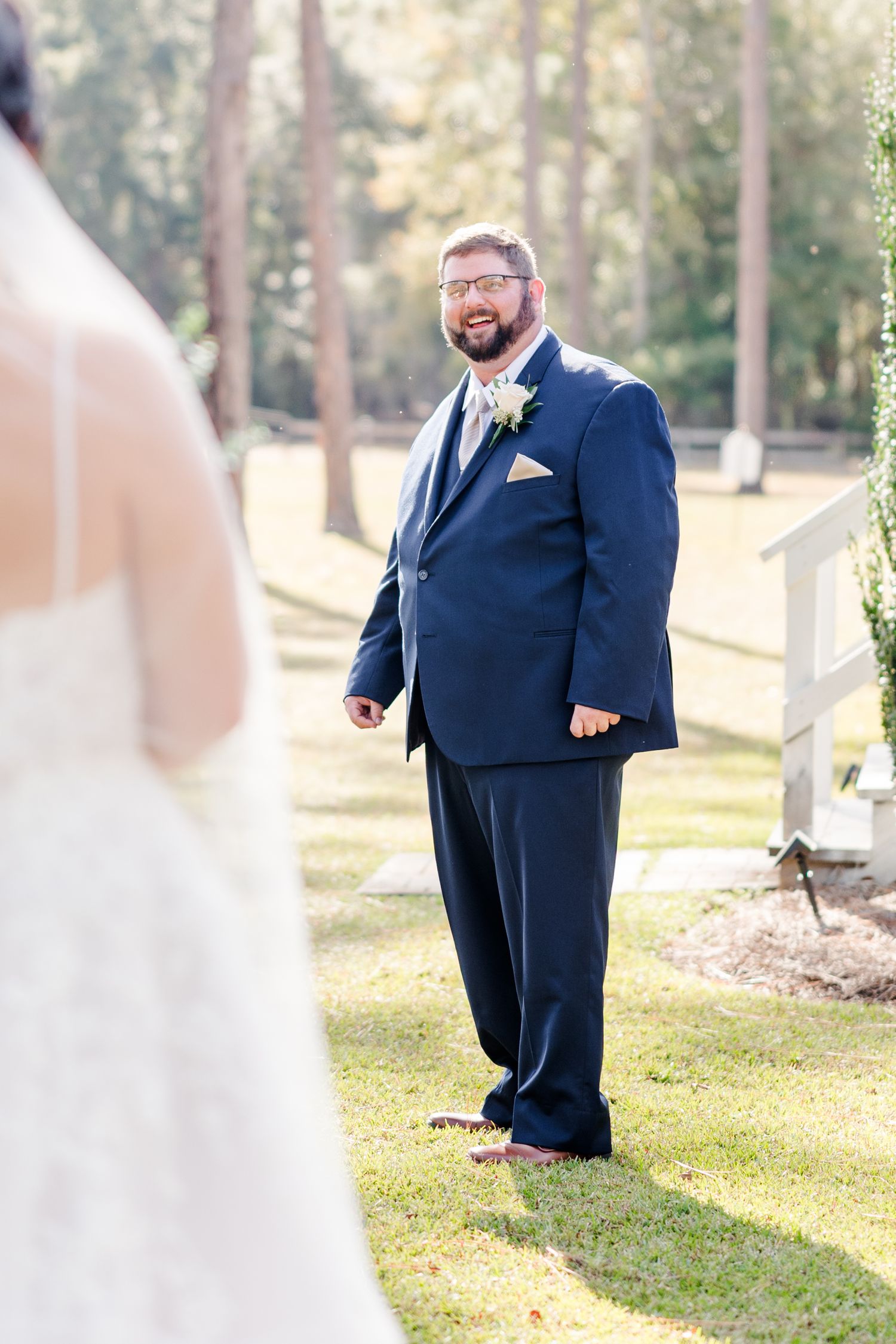 Groom in navy suit reacts emotionally during first look with bride in outdoor setting.