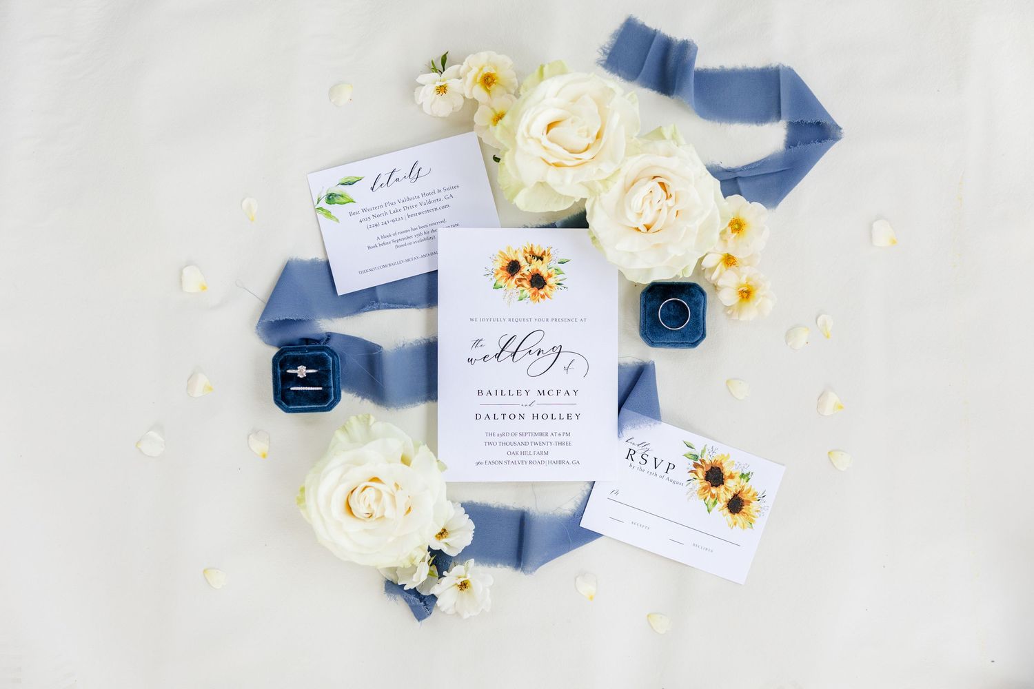 Wedding invitation suite with white roses, blue ribbon, and elegant stationery on white background.