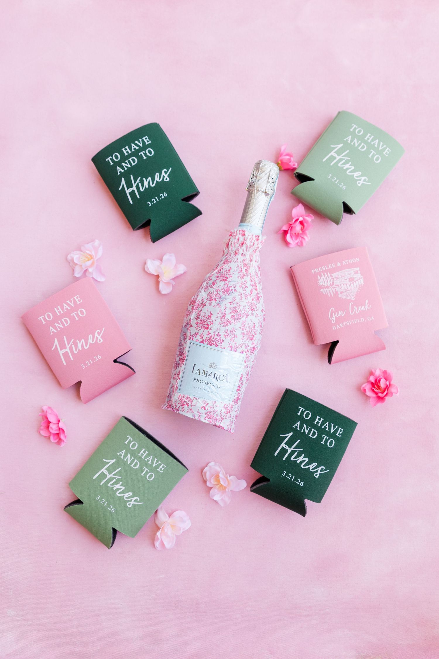 Pink and green custom wedding koozies surrounding a floral champagne bottle on a pink background.