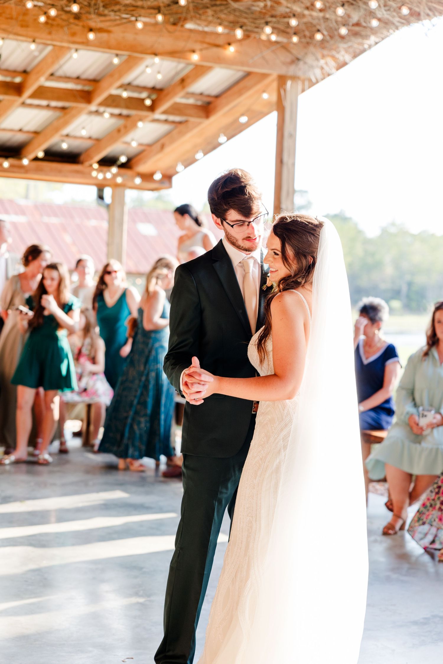 Bride and groom share their first dance under string lights at a rustic outdoor wedding reception.