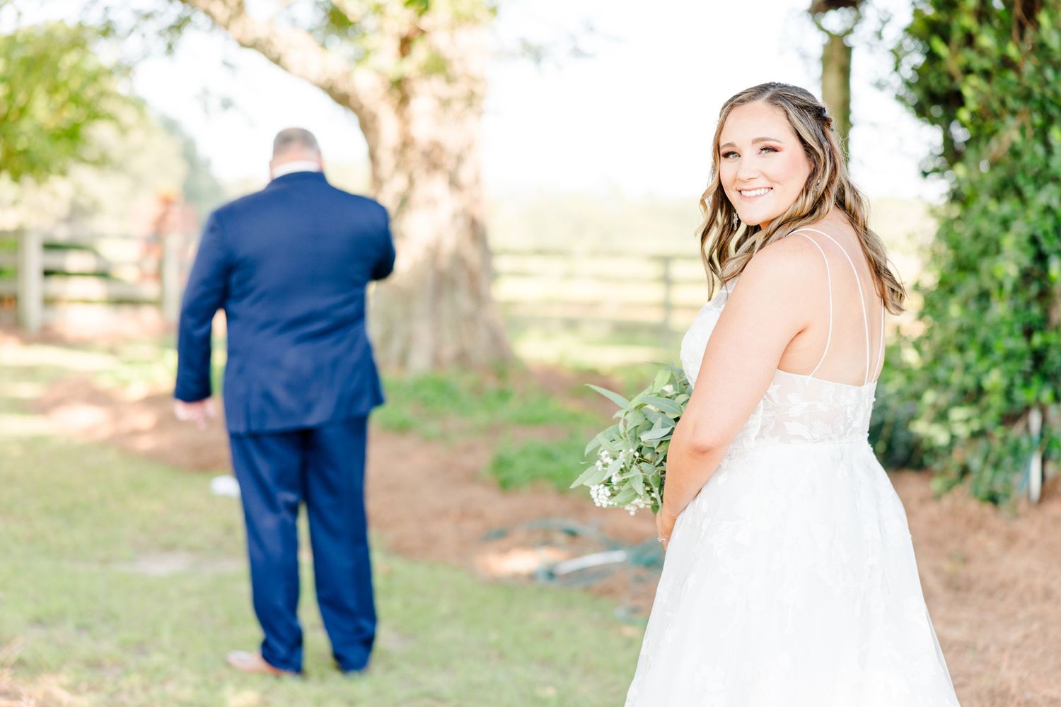Wedding couple sharing their first look moment under trees in a sunlit garden.