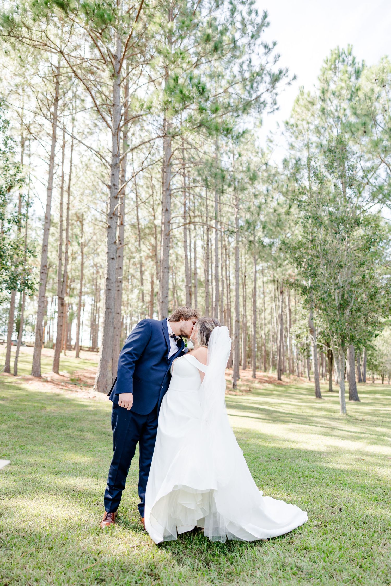 Full-length wedding portrait of couple in pine forest setting with natural lighting.