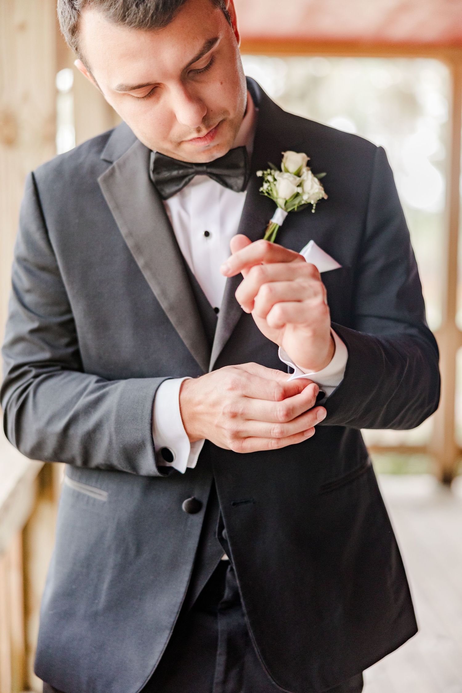 Groom in black tuxedo adjusting white boutonniere.