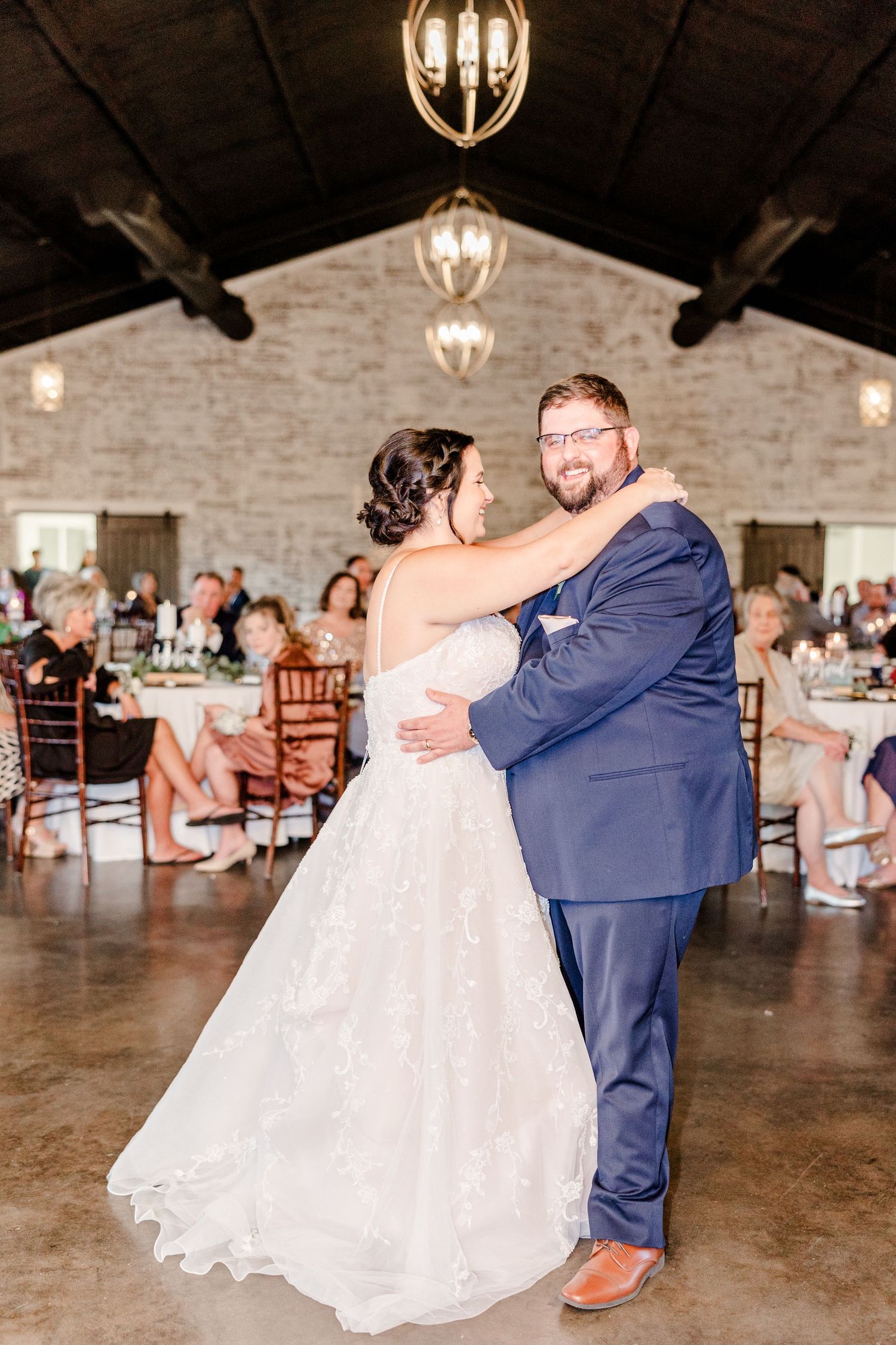 Wedding couple performs romantic dance dip in rustic stone venue with chandeliers.