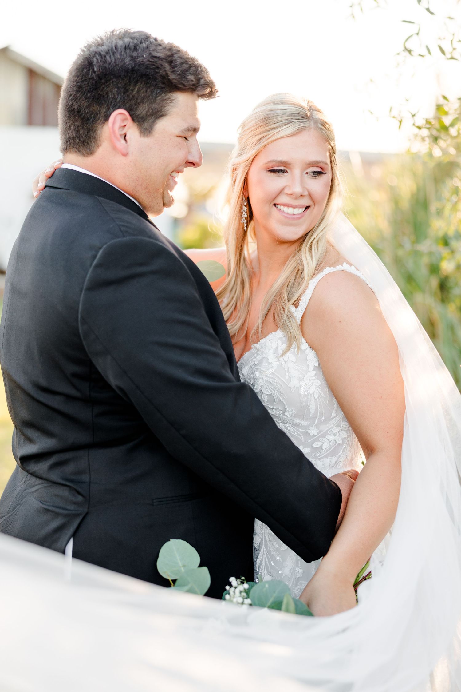 A romantic outdoor wedding portrait of a couple sharing a joyful moment in golden sunlight.