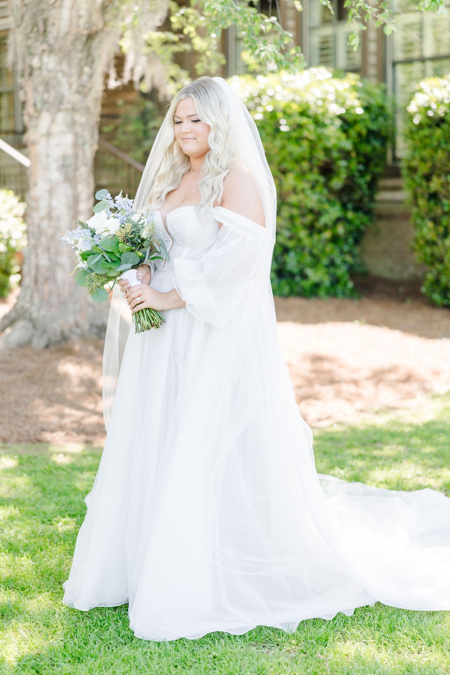 Elegant white wedding dress with flowing train displayed in a sunlit garden setting.