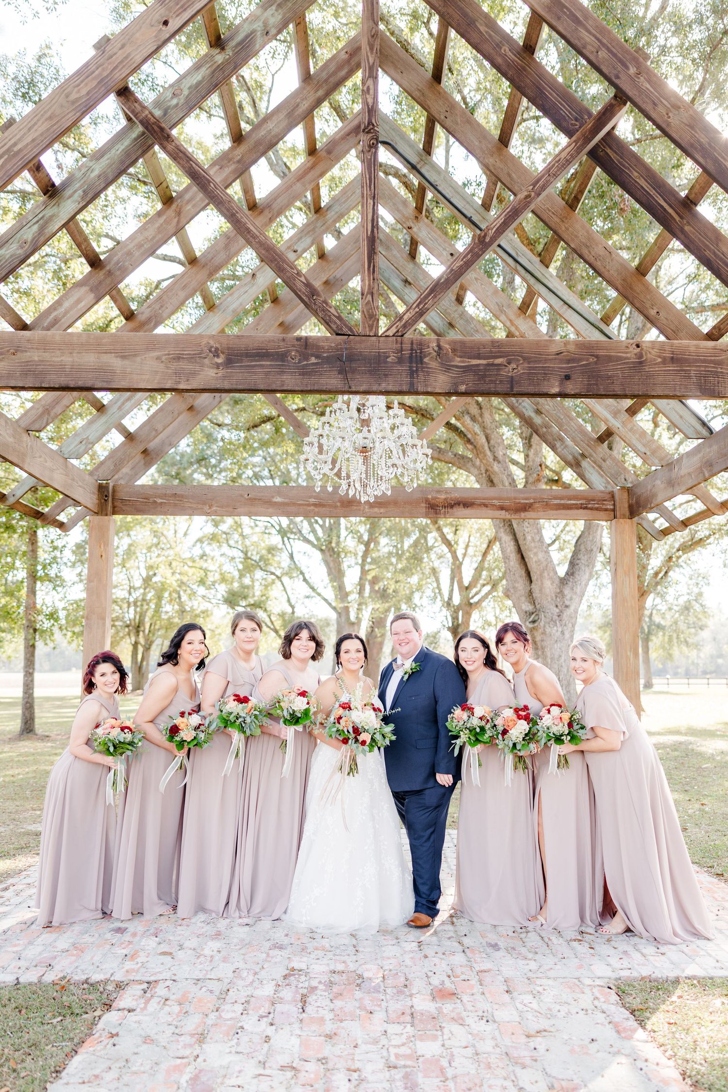 Wedding party poses under rustic wooden pergola with chandelier decoration.