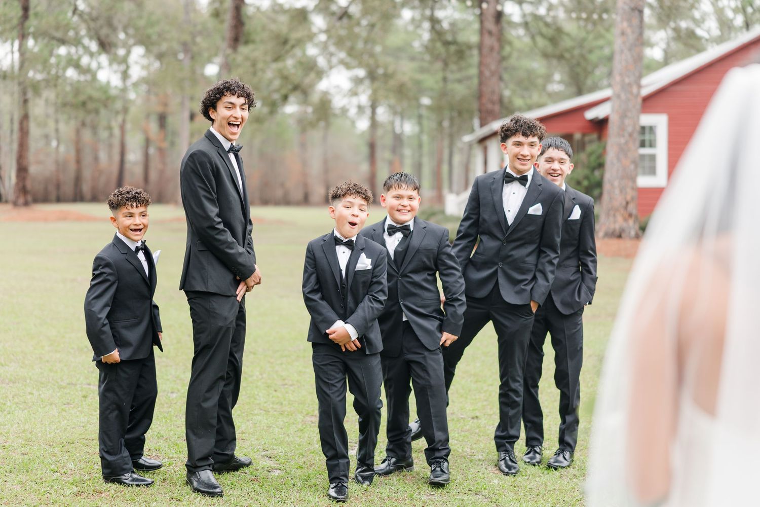 Groomsmen in matching black suits run playfully across a grassy outdoor venue.