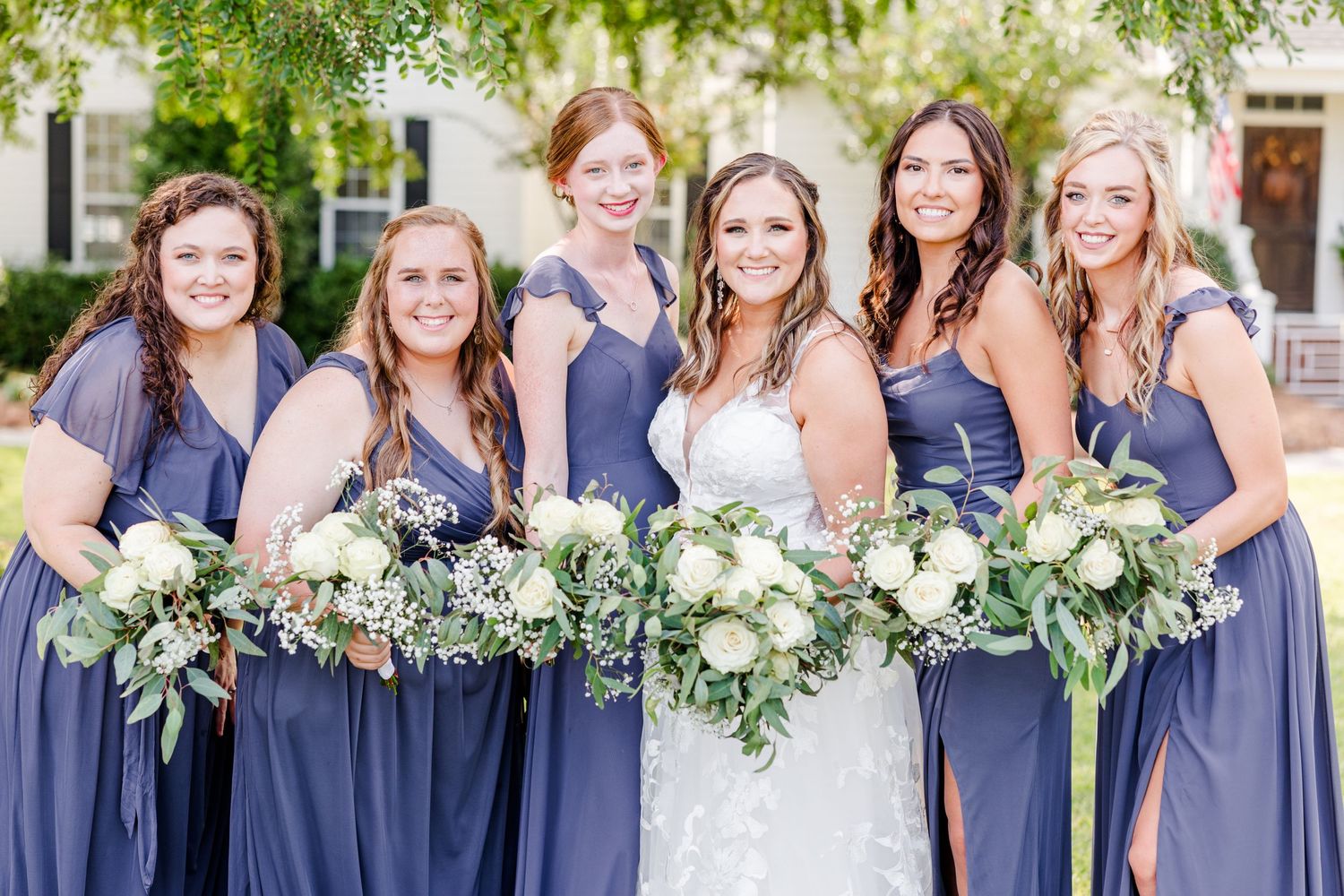 Bridesmaids in matching blue dresses line up for formal wedding photos.
