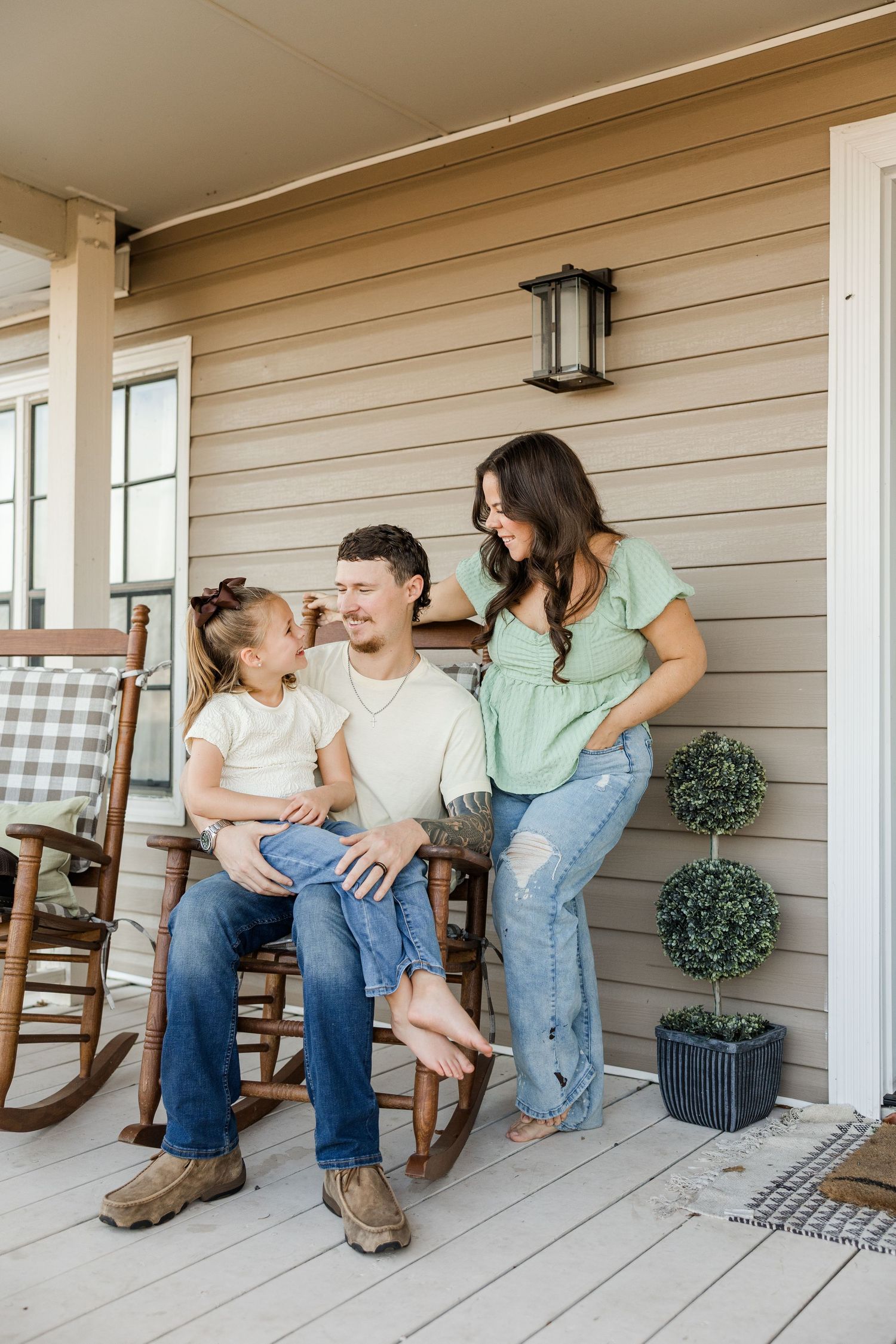 A happy family of three sits on a cozy porch with rocking chairs, sharing a joyful moment together.