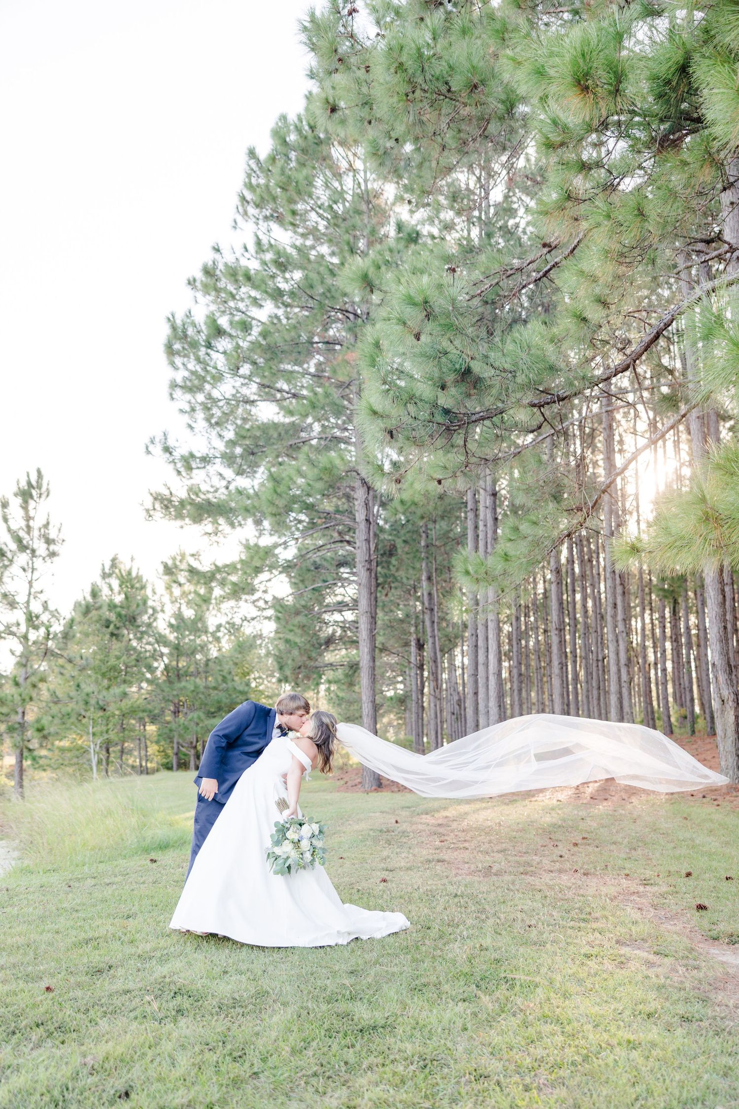 Wedding couple photographed in pine forest with flowing white dress and natural lighting.