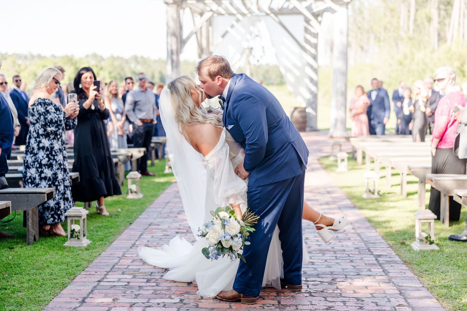 Romantic outdoor wedding ceremony with guests seated on wooden chairs along a stone pathway.