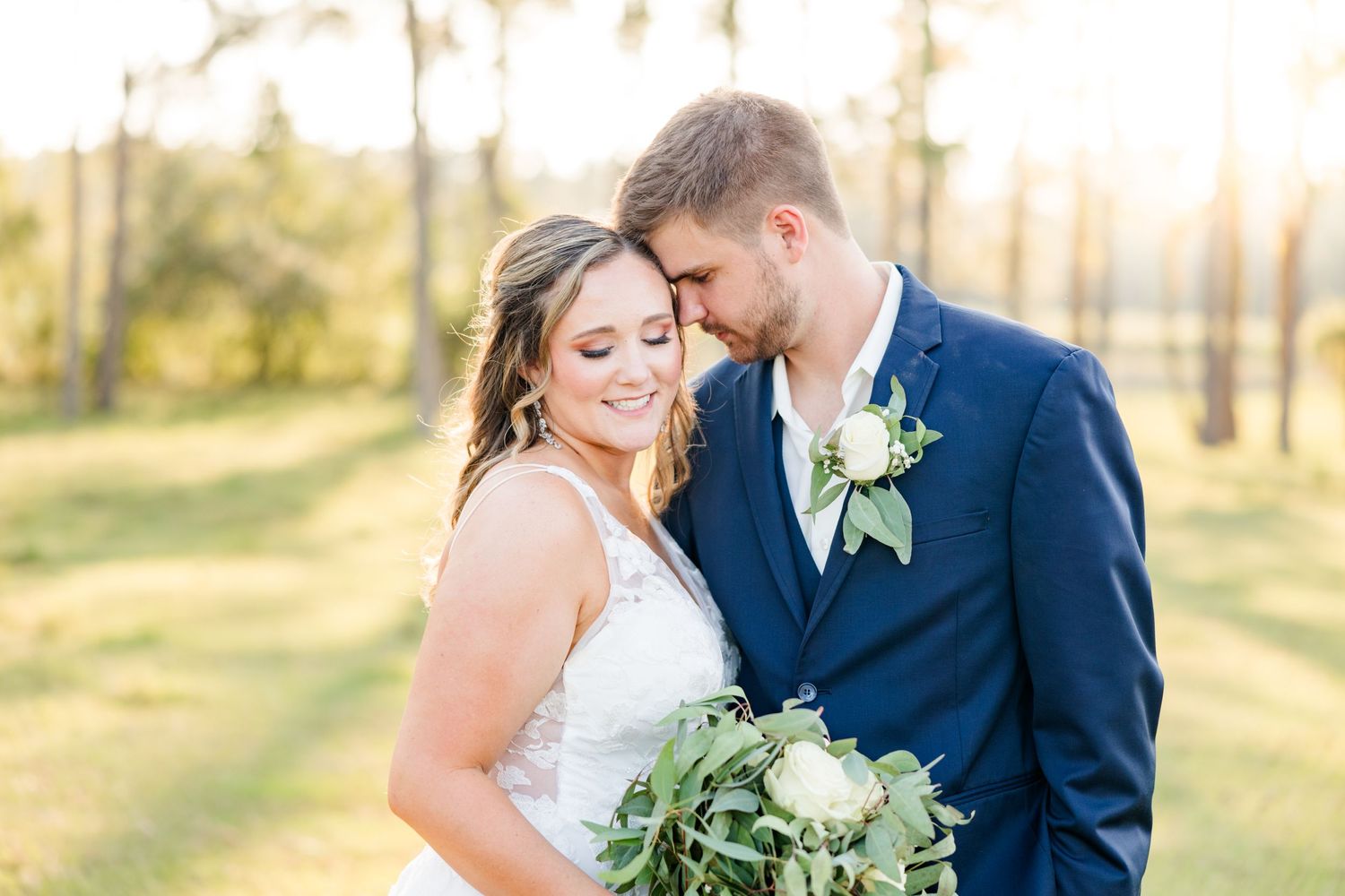 A tender wedding moment photographed in warm evening light among tall pine trees.