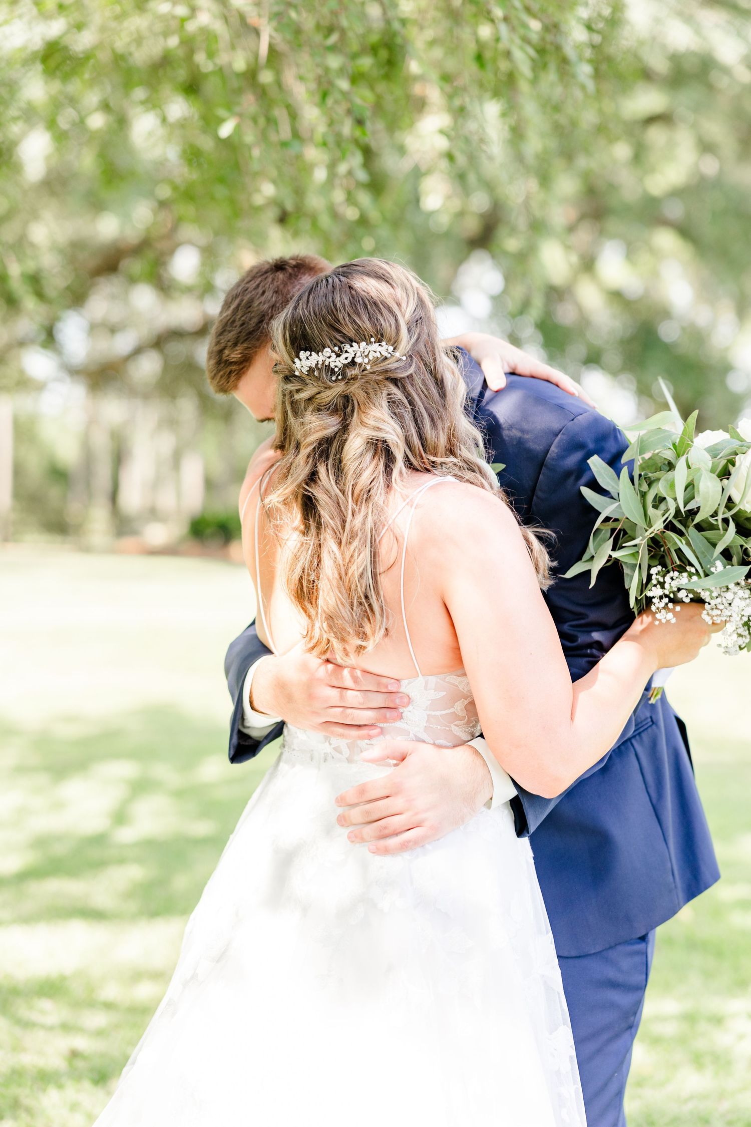 Bride in white gown and groom in navy suit embrace during their outdoor wedding photoshoot.