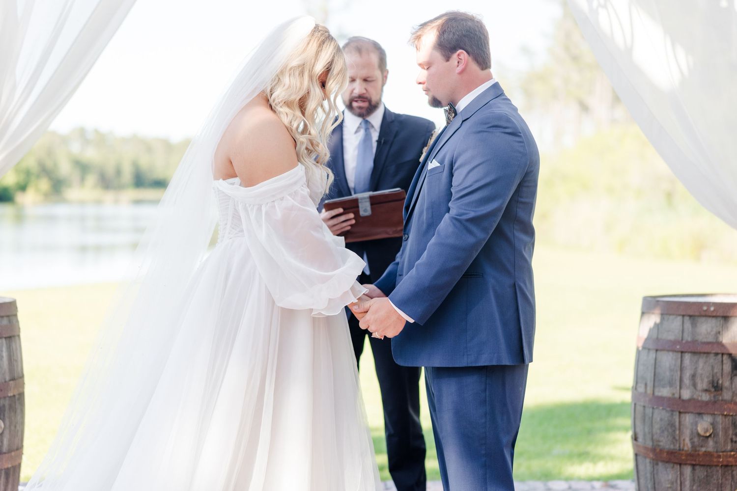Intimate wedding ceremony moment under a white draped pavilion by the water.