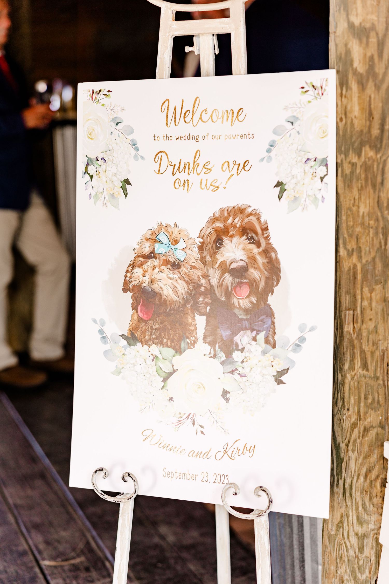 Wedding welcome signs with floral designs and gold lettering displayed on wooden stands.