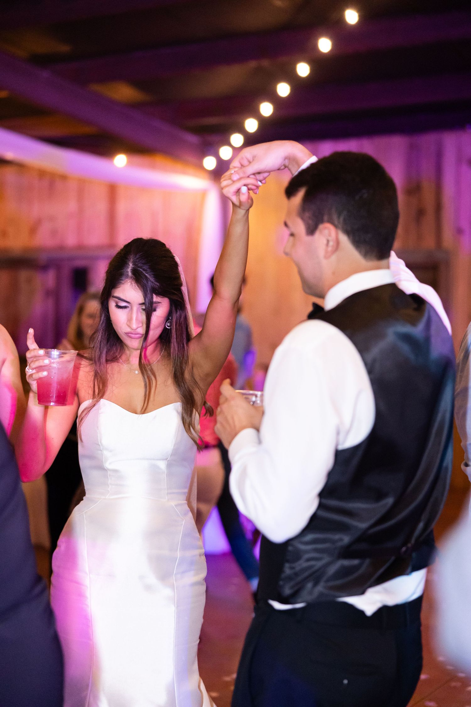 Dancing at wedding reception with colorful lighting and rustic barn backdrop.