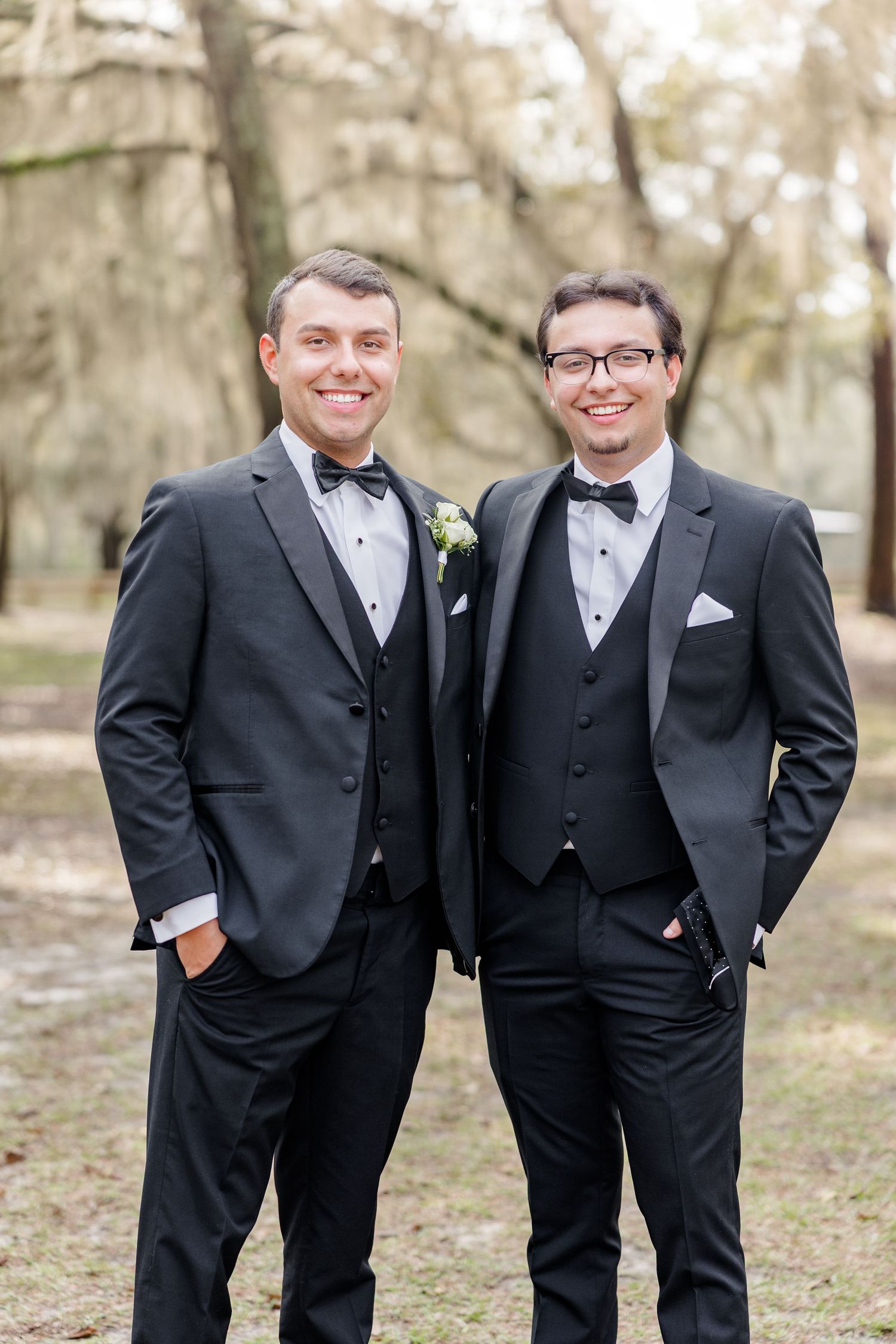 Groomsmen in classic black tuxedos pose together in an outdoor setting with natural lighting.