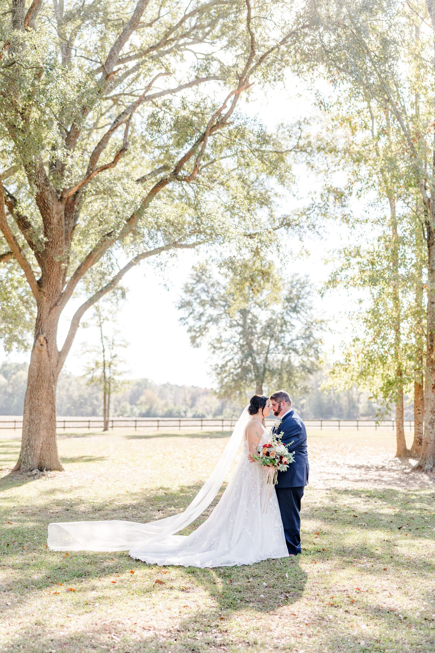 Newlyweds pose under large trees in romantic outdoor wedding portraits.