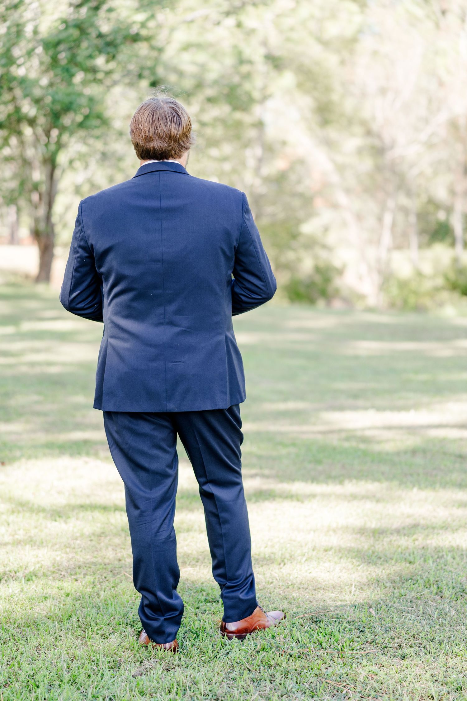 Five figures in navy suits stand at different distances on a grassy lawn.