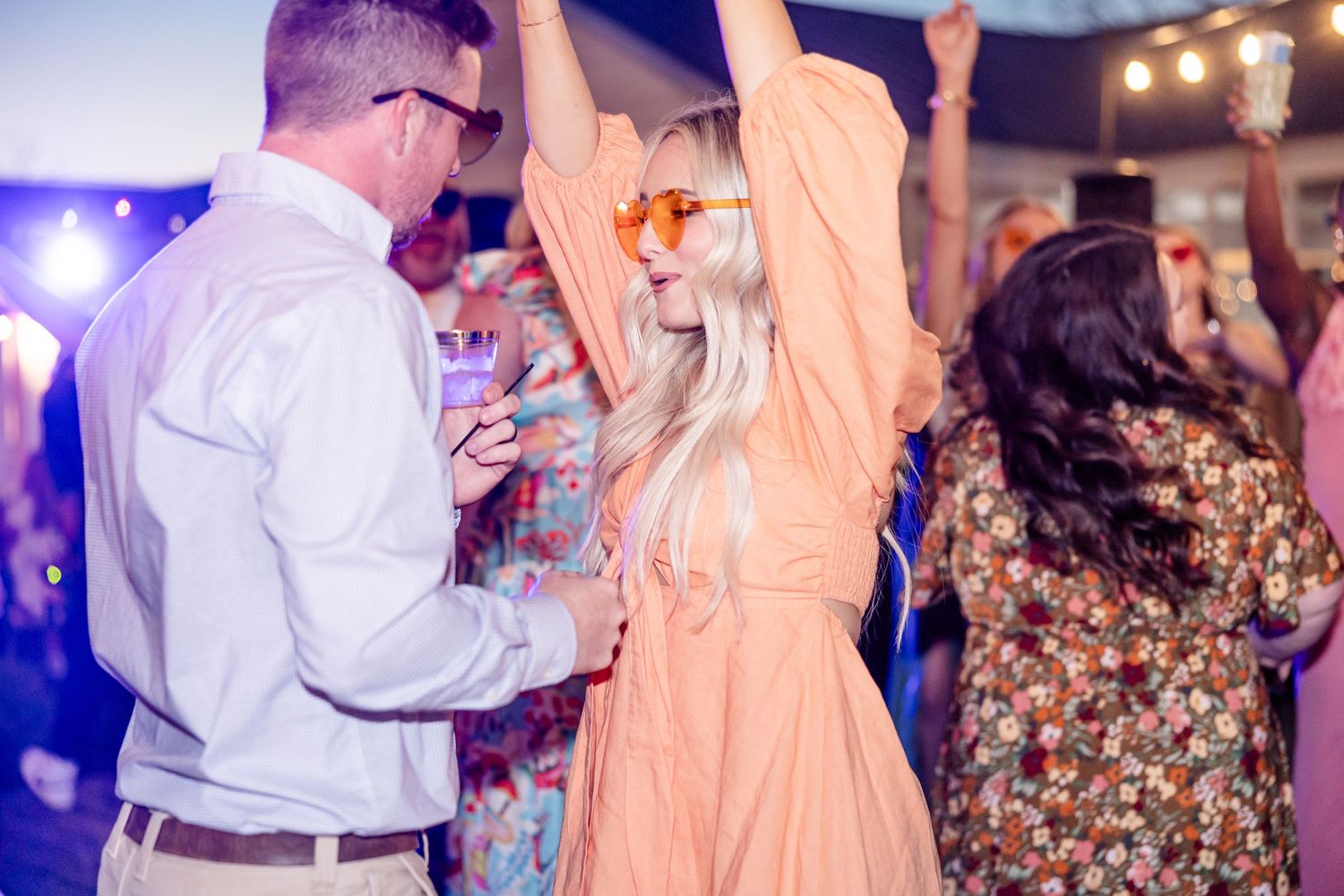 Party guests dancing and celebrating under purple lighting at a reception event.