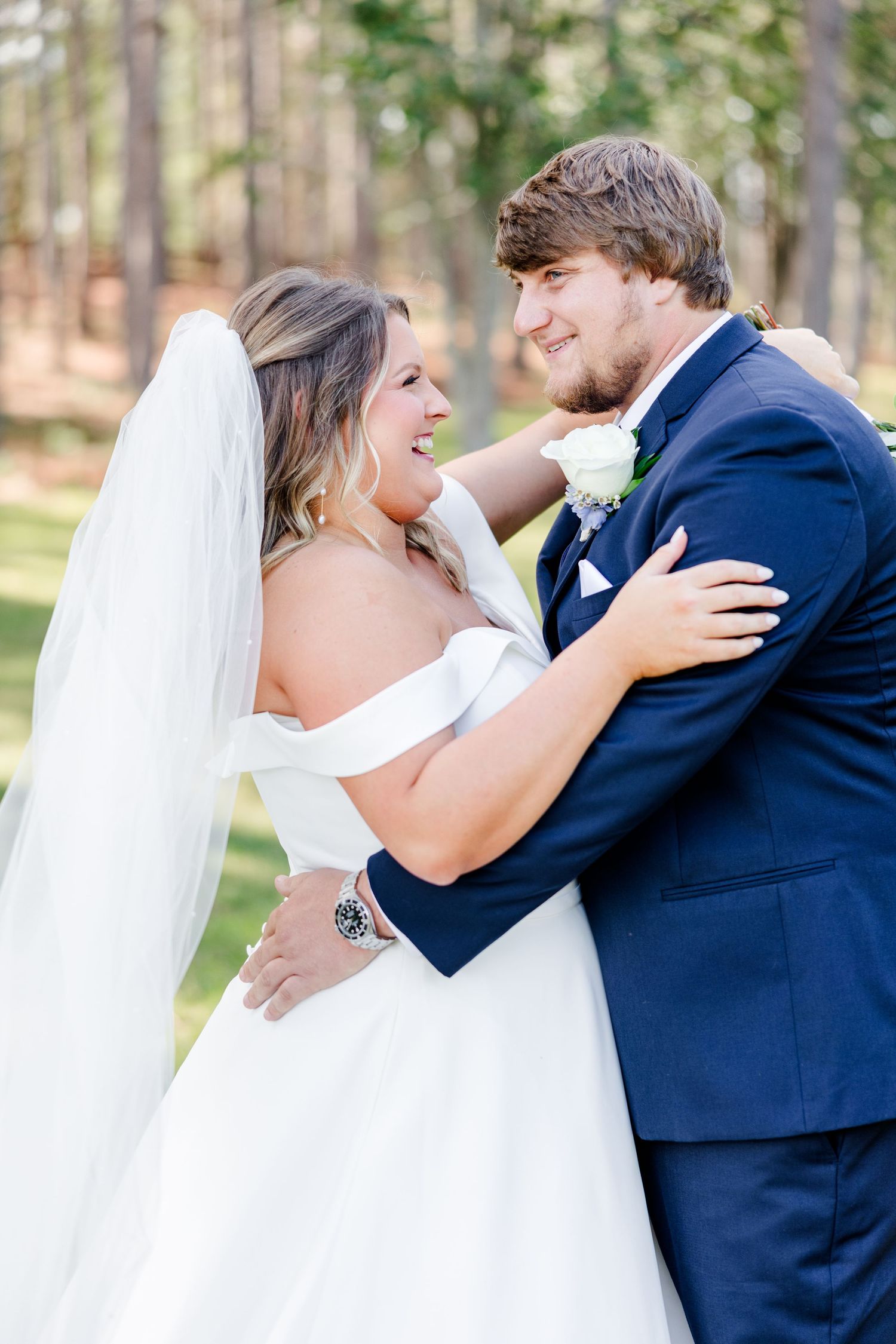 A romantic wedding moment between newlyweds in a forest setting with the bride in white and groom in navy.