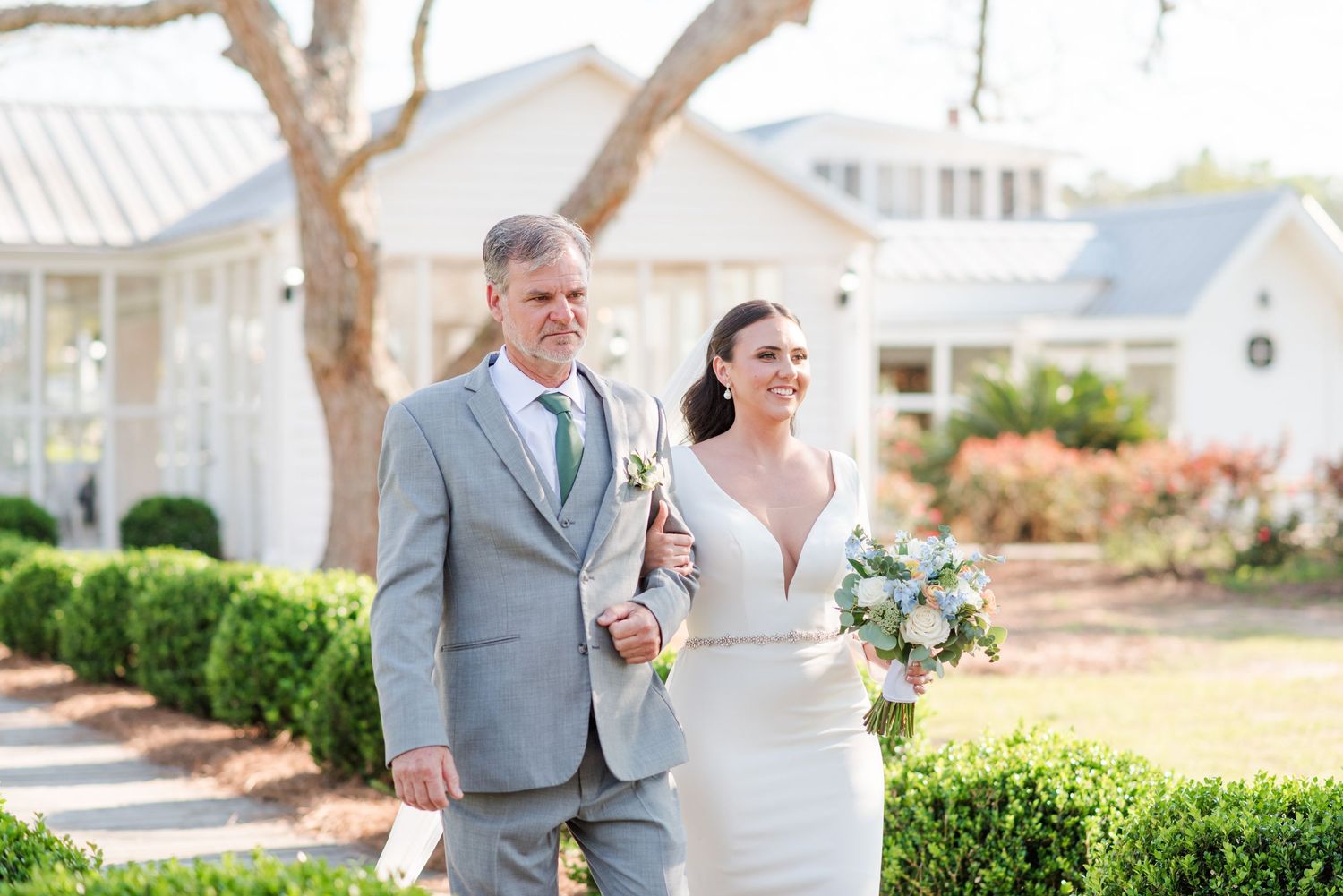 A couple poses for wedding portraits outside a classic white wedding venue.