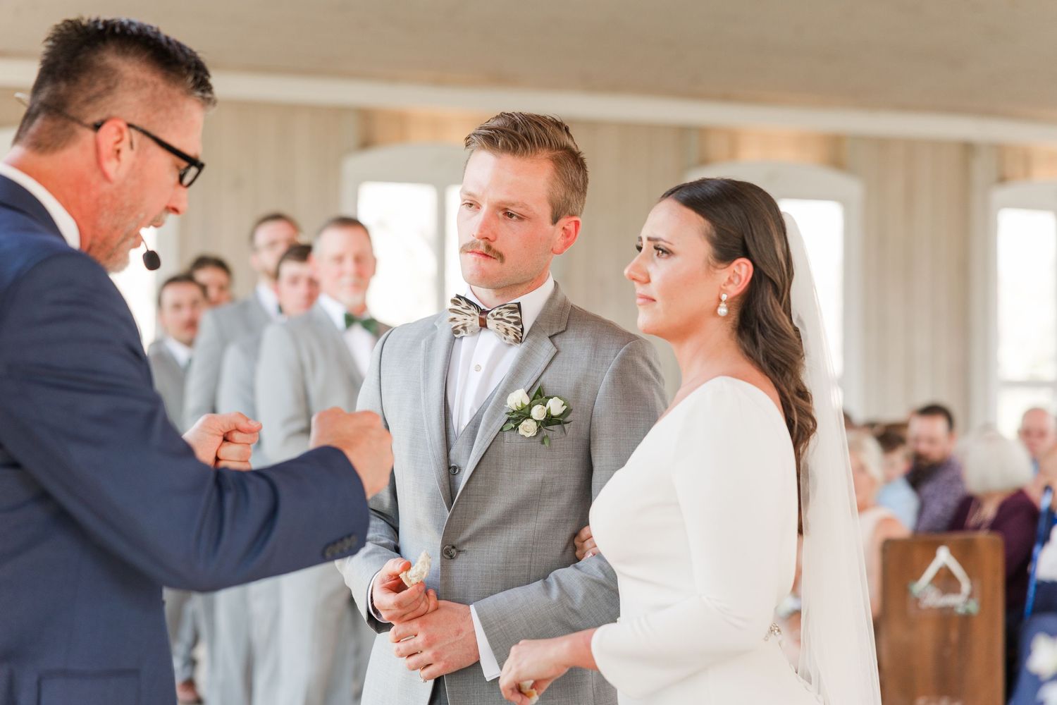 Wedding party in grey suits and white dresses dancing together in a bright indoor venue.