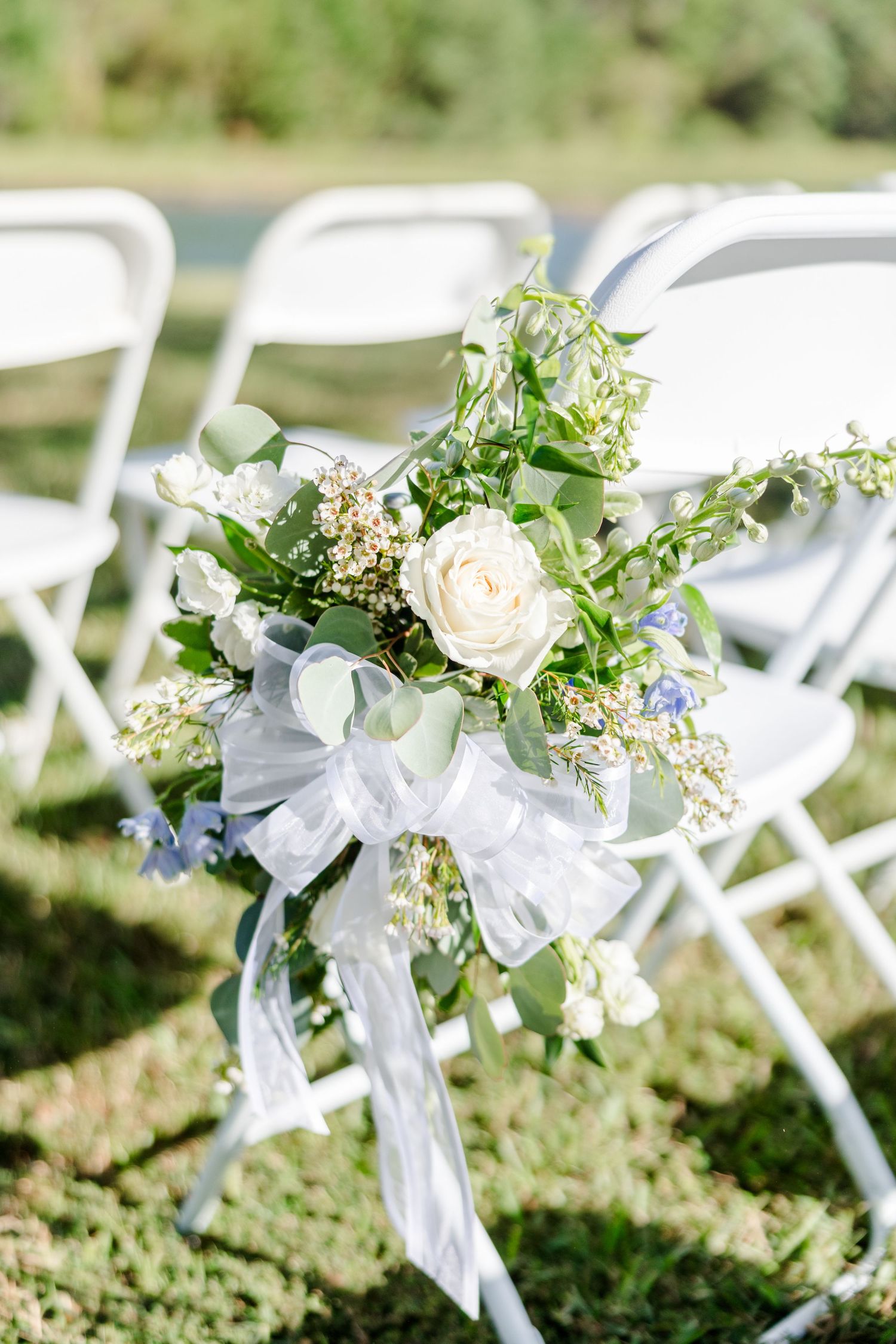 White floral and greenery decorations adorn ceremony chairs with delicate ribbon accents.