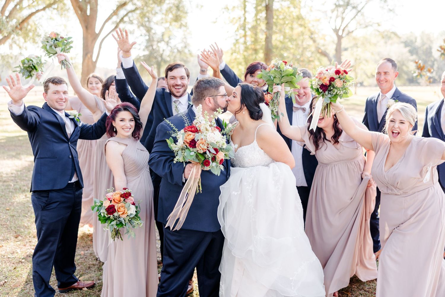 Wedding party celebrates joyfully outdoors in navy and blush pink attire.