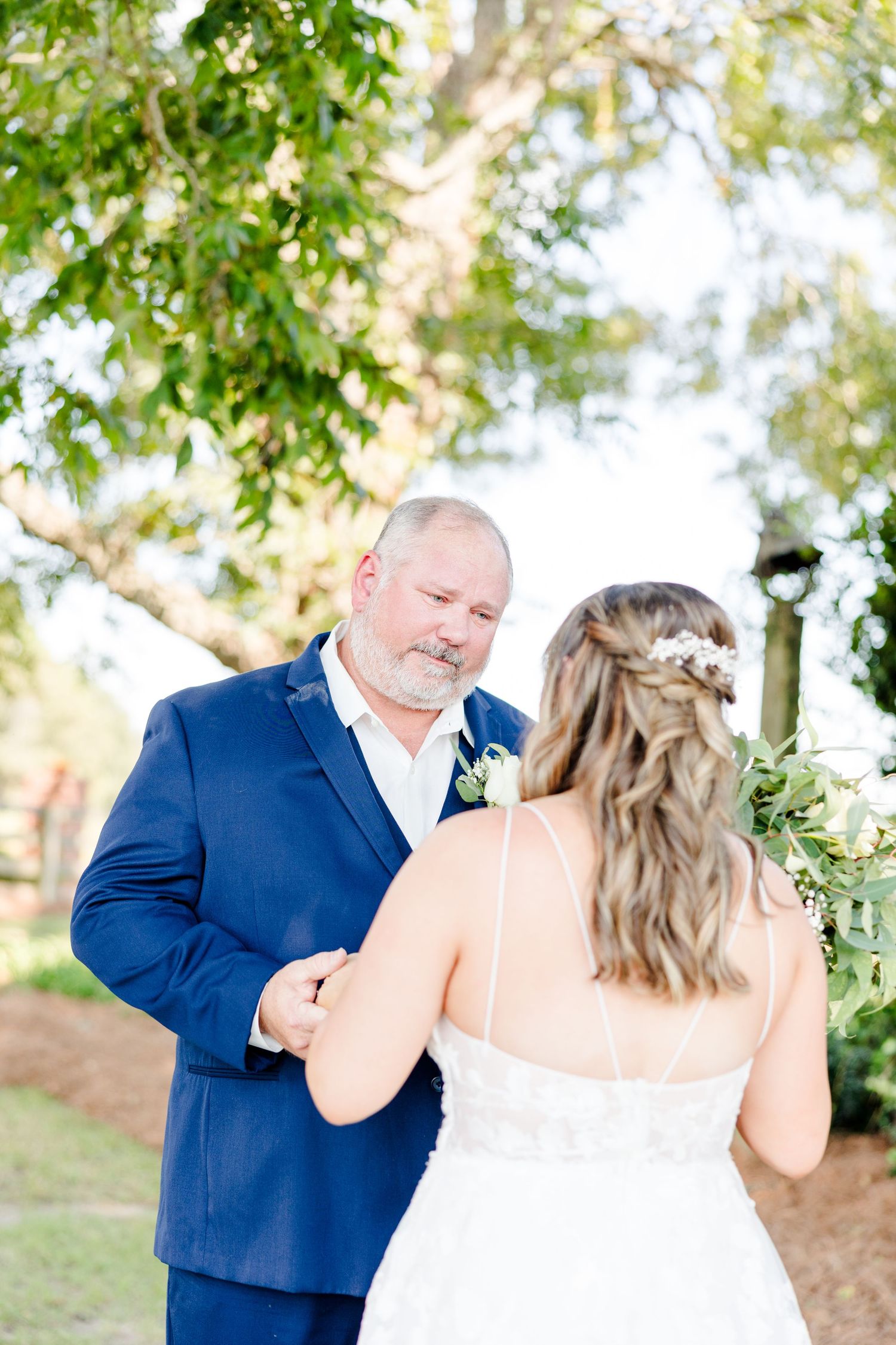 Wedding couple sharing intimate first look moment under trees with natural lighting.
