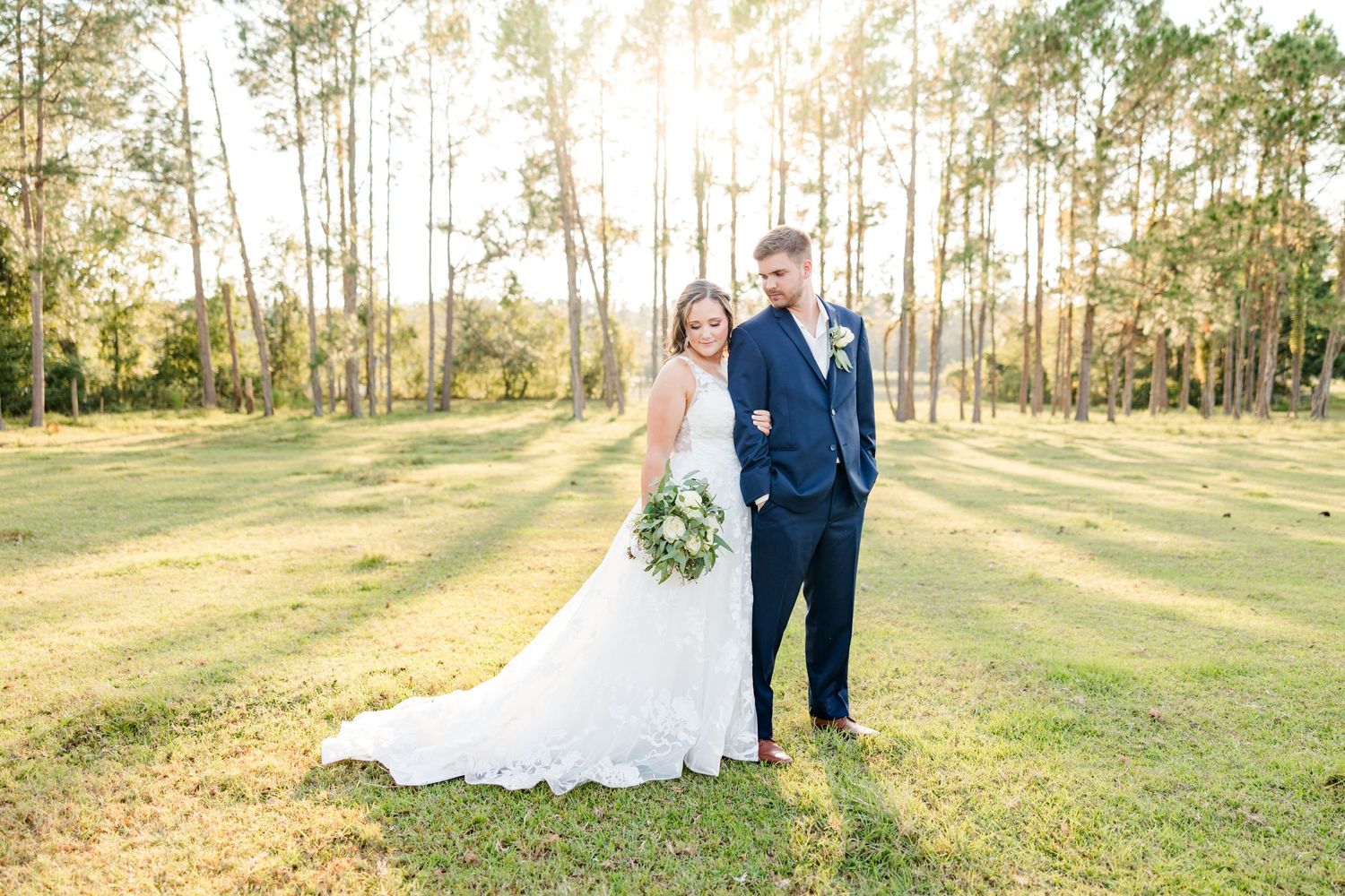 A sunlit wedding portrait in a natural pine forest setting with golden afternoon light.