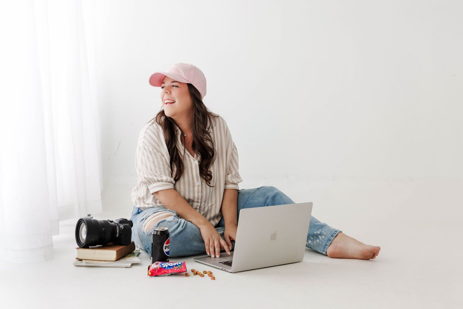 Photographer in casual attire works with camera and laptop in minimalist setting.