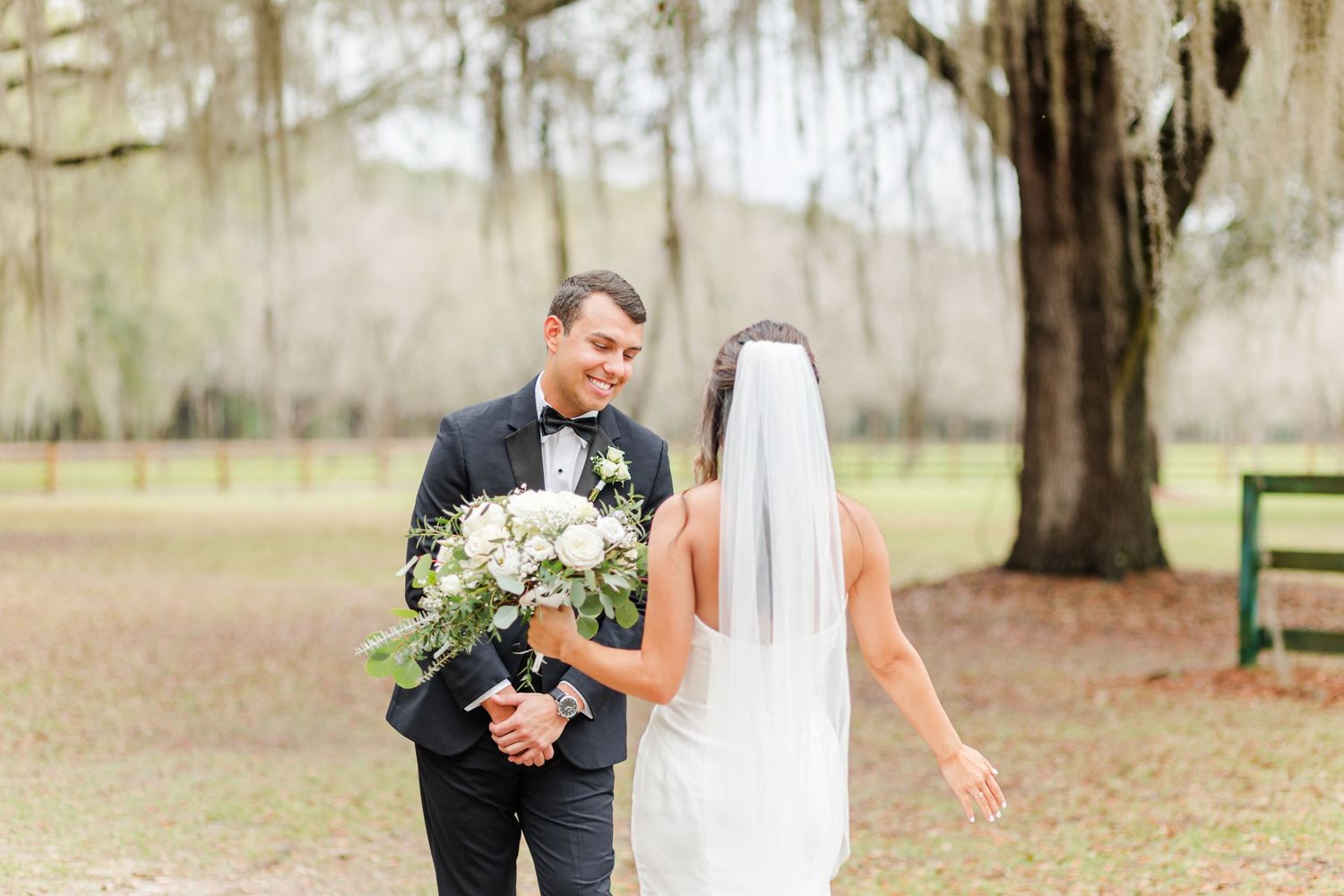 A couple shares their first look moment in a rustic outdoor setting with Spanish moss trees.