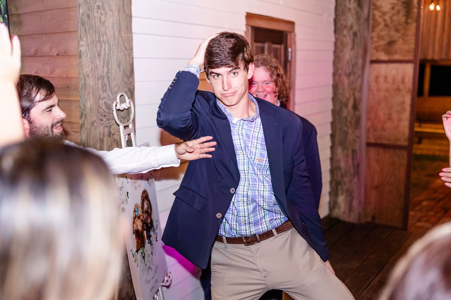 Wedding guests dancing enthusiastically on a dimly lit dance floor at an indoor reception venue.
