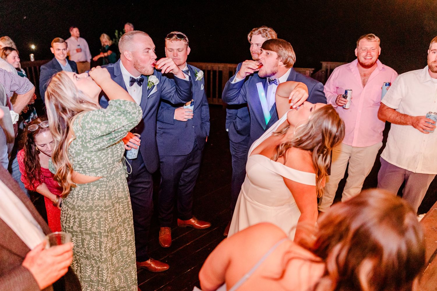Wedding guests dance and celebrate on a dimly lit dance floor during the reception.