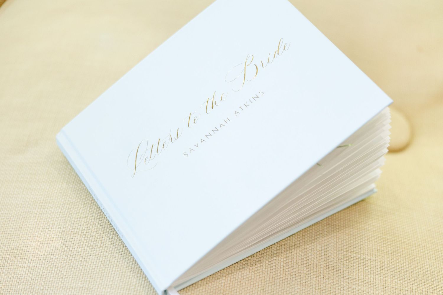 Elegant white wedding guest book or invitation cards displayed on beige linen background.