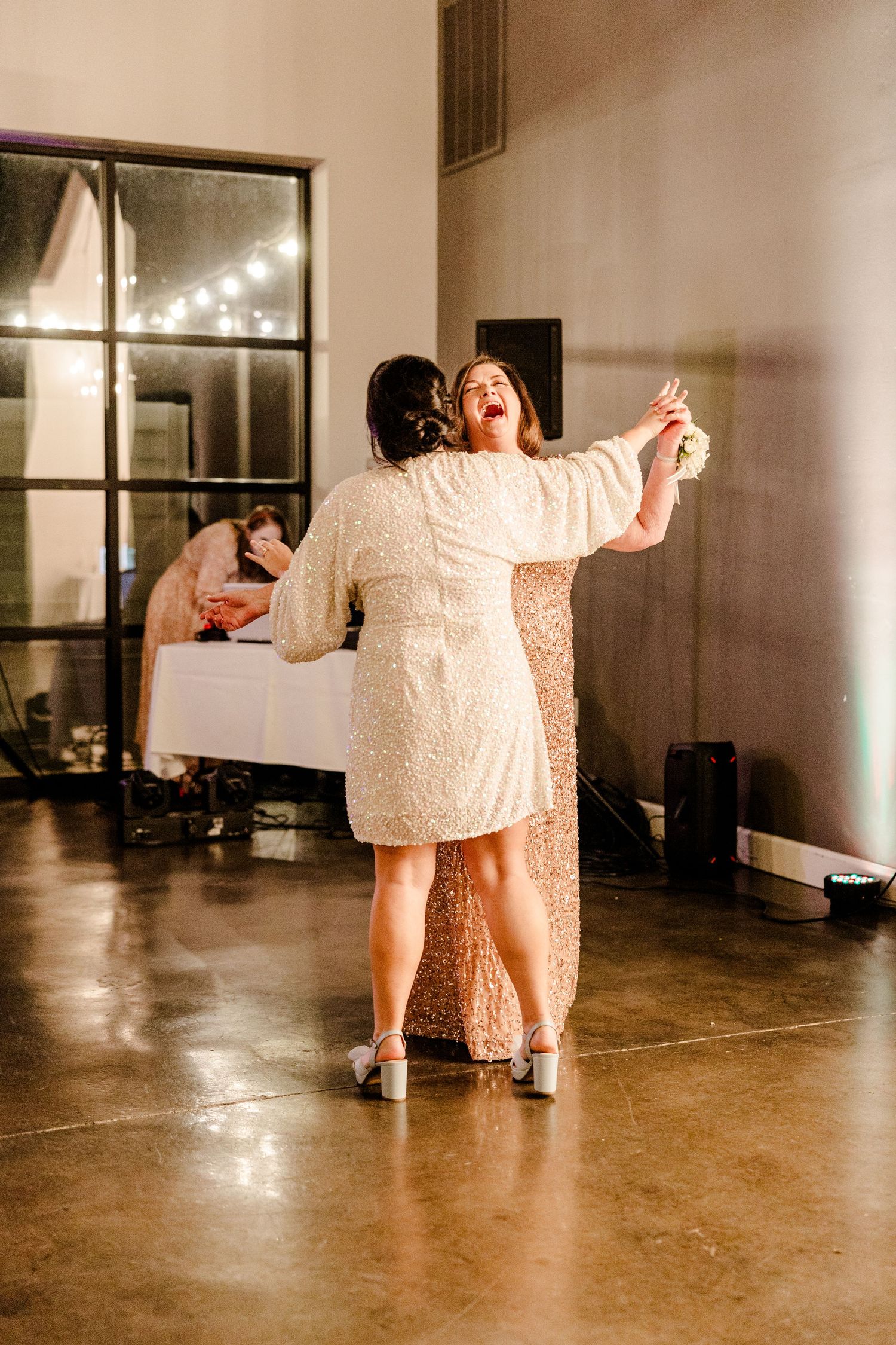Wedding guests dancing on polished concrete floor in dimly lit reception space.